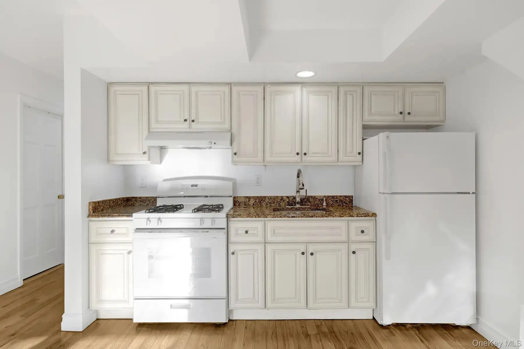 Kitchen featuring white appliances, dark stone countertops, light wood-type flooring, and under cabinet range hood Kitchen featuring white appliances, dark stone countertops, light wood-type flooring, and under cabinet range hood