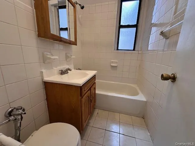 Bathroom featuring tile walls, vanity, shower combination, light tile patterned flooring, and healthy amount of natural light Bathroom featuring tile walls, vanity, shower combination, light tile patterned flooring, and healthy amount of natural light