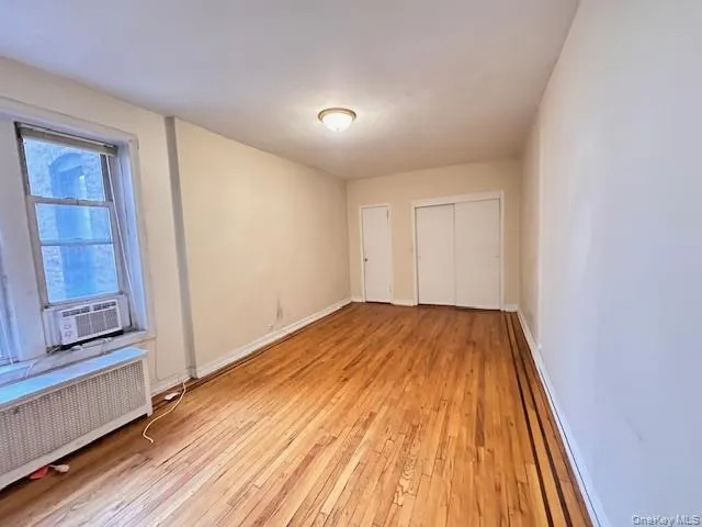 Unfurnished studio with radiator, light wood finished floors, a baseboard heating unit, and cooling unit Unfurnished studio with radiator, light wood finished floors, a baseboard heating unit, and cooling unit