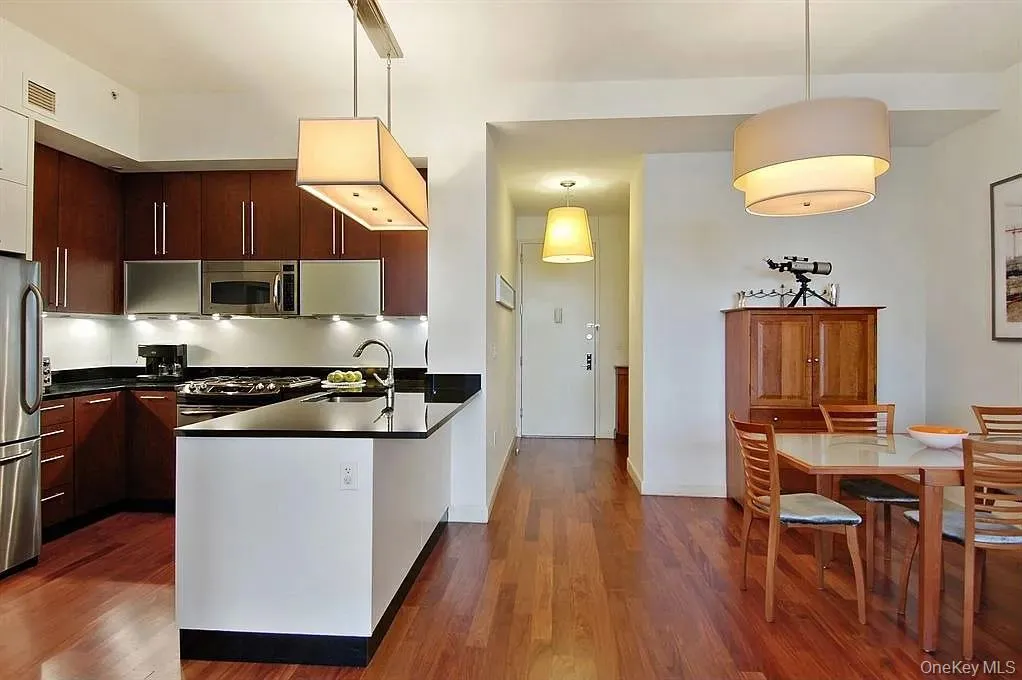 Kitchen with appliances with stainless steel finishes, a peninsula, decorative light fixtures, dark wood-type flooring, and modern cabinets Kitchen with appliances with stainless steel finishes, a peninsula, decorative light fixtures, dark wood-type flooring, and modern cabinets