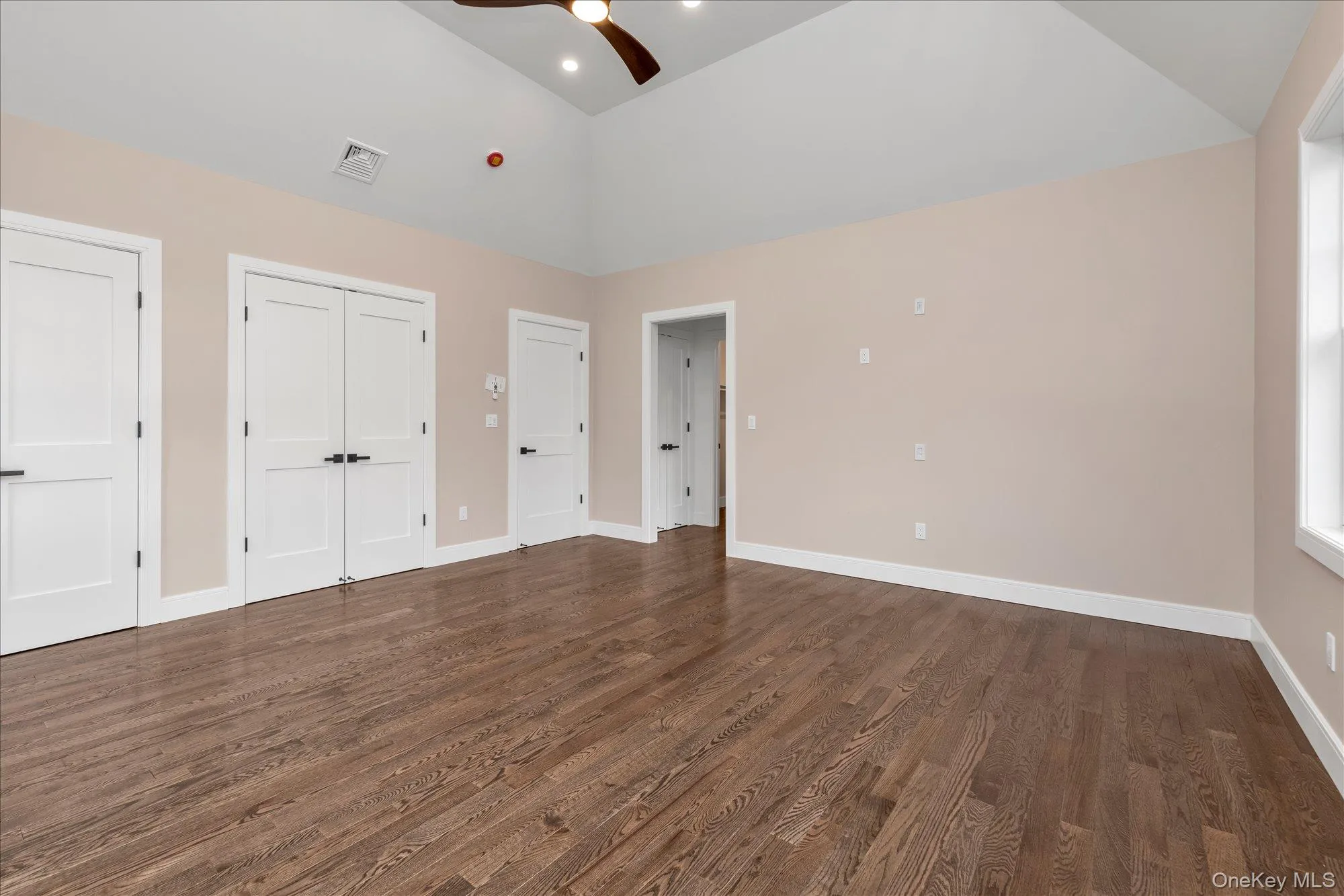Unfurnished bedroom featuring dark wood-style floors, two closets, high vaulted ceiling, and a ceiling fan Unfurnished bedroom featuring dark wood-style floors, two closets, high vaulted ceiling, and a ceiling fan