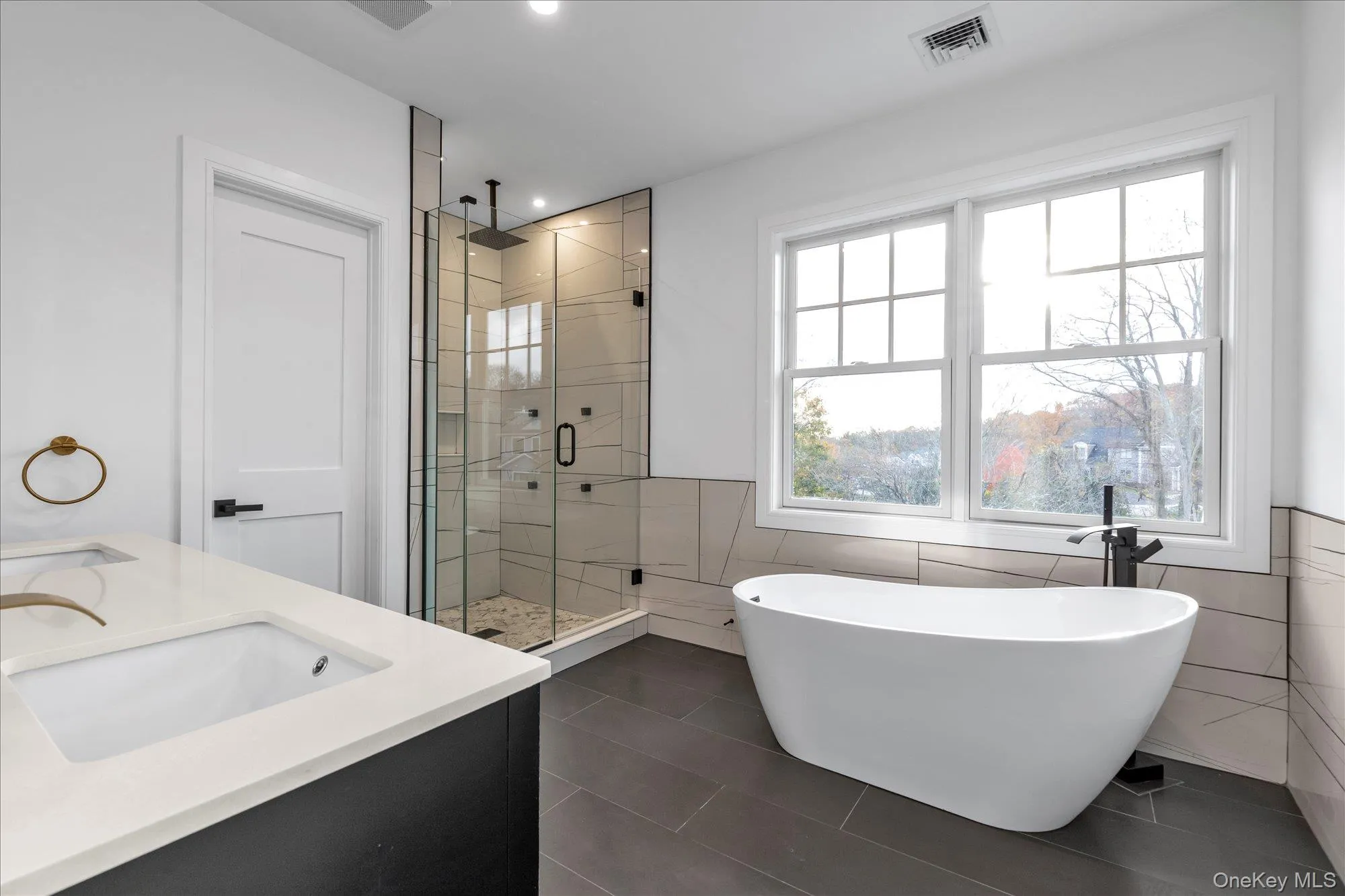 Bathroom with a freestanding bath, double vanity, a stall shower, tile walls, and dark tile patterned flooring Bathroom with a freestanding bath, double vanity, a stall shower, tile walls, and dark tile patterned flooring