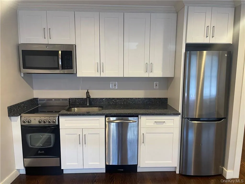 Kitchen featuring stainless steel appliances, white cabinets, dark stone counters, and dark wood-type flooring Kitchen featuring stainless steel appliances, white cabinets, dark stone counters, and dark wood-type flooring