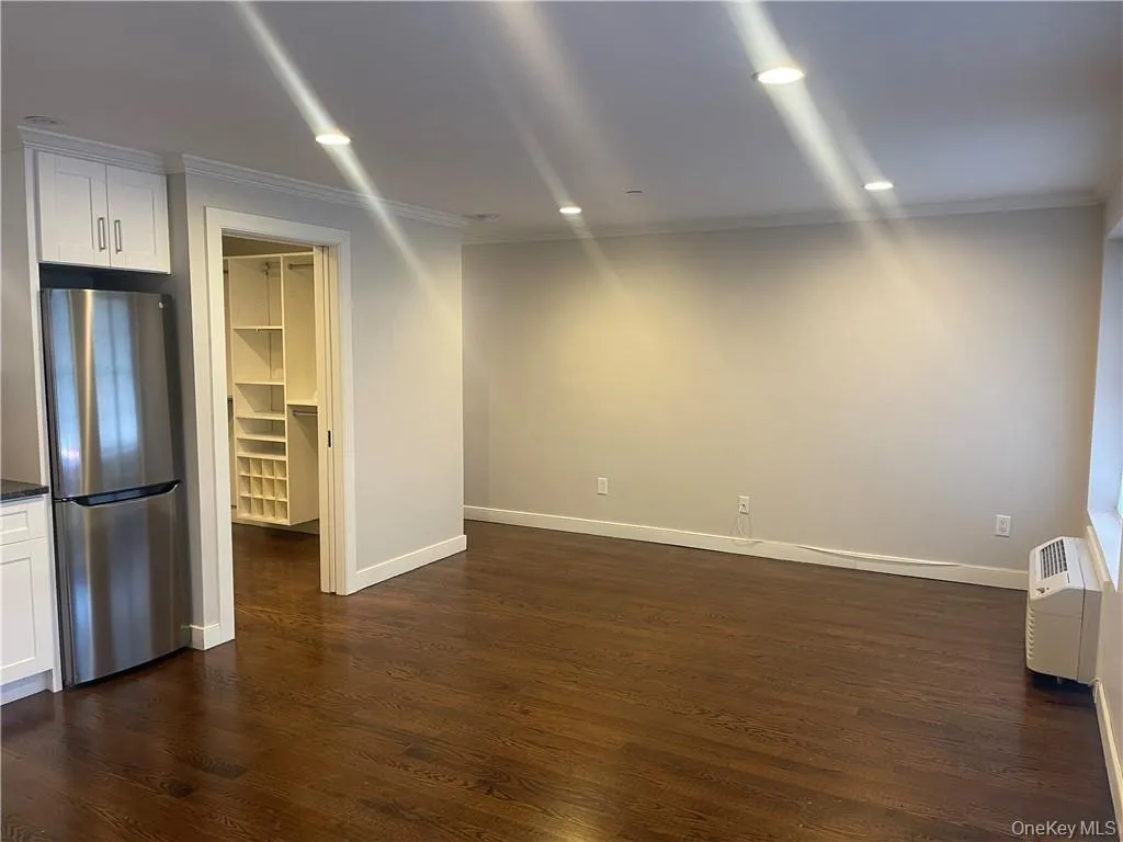 Unfurnished room featuring crown molding, dark wood-style flooring, recessed lighting, and a wall mounted air conditioner Unfurnished room featuring crown molding, dark wood-style flooring, recessed lighting, and a wall mounted air conditioner