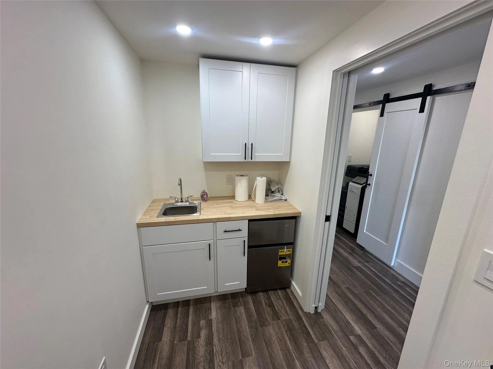Bar area with a barn door, stainless steel fridge, white cabinetry, dark wood-style flooring, and recessed lighting Bar area with a barn door, stainless steel fridge, white cabinetry, dark wood-style flooring, and recessed lighting