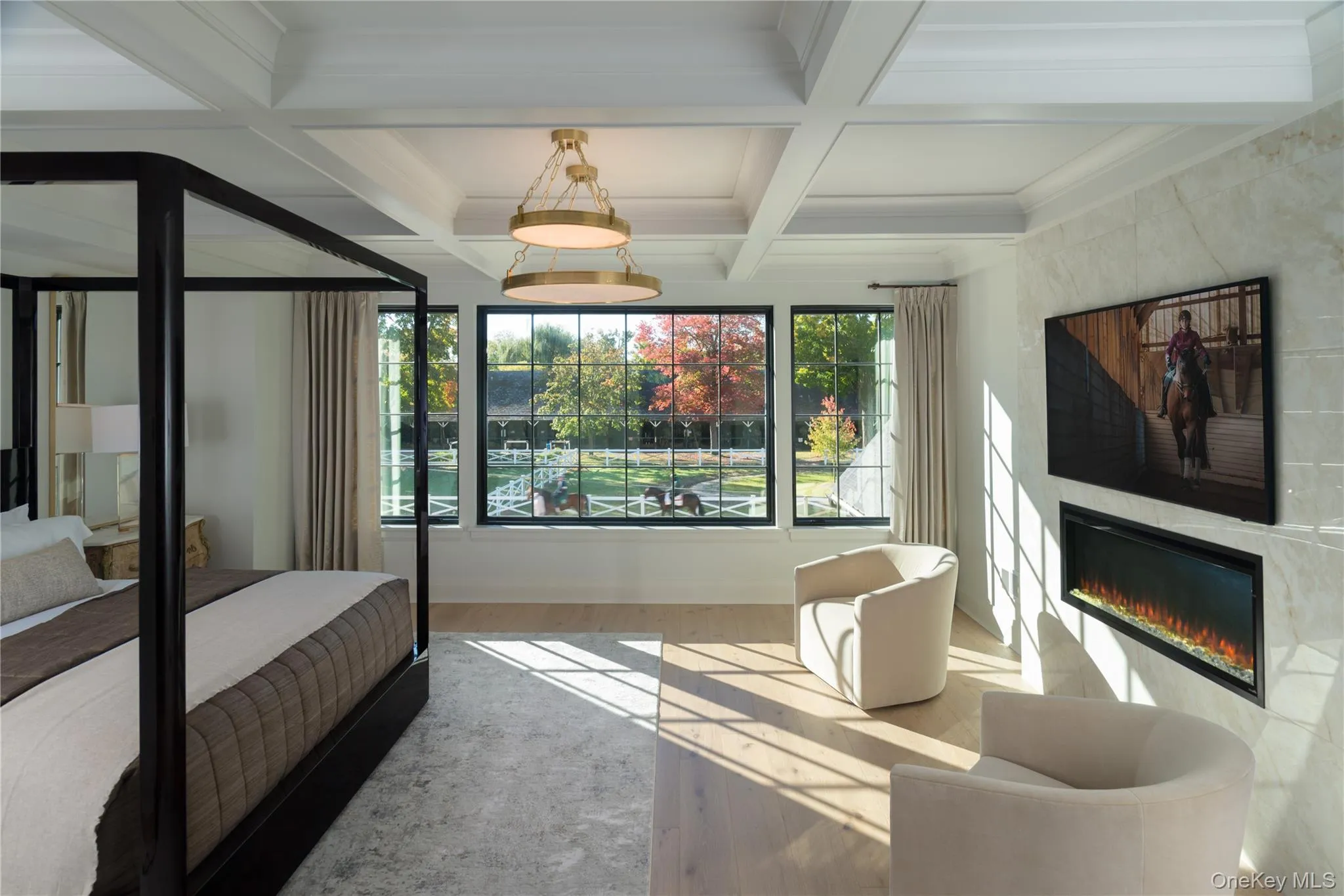 Bedroom featuring beamed ceiling, coffered ceiling, a glass covered fireplace, ornamental molding, and wood finished floors Bedroom featuring beamed ceiling, coffered ceiling, a glass covered fireplace, ornamental molding, and wood finished floors