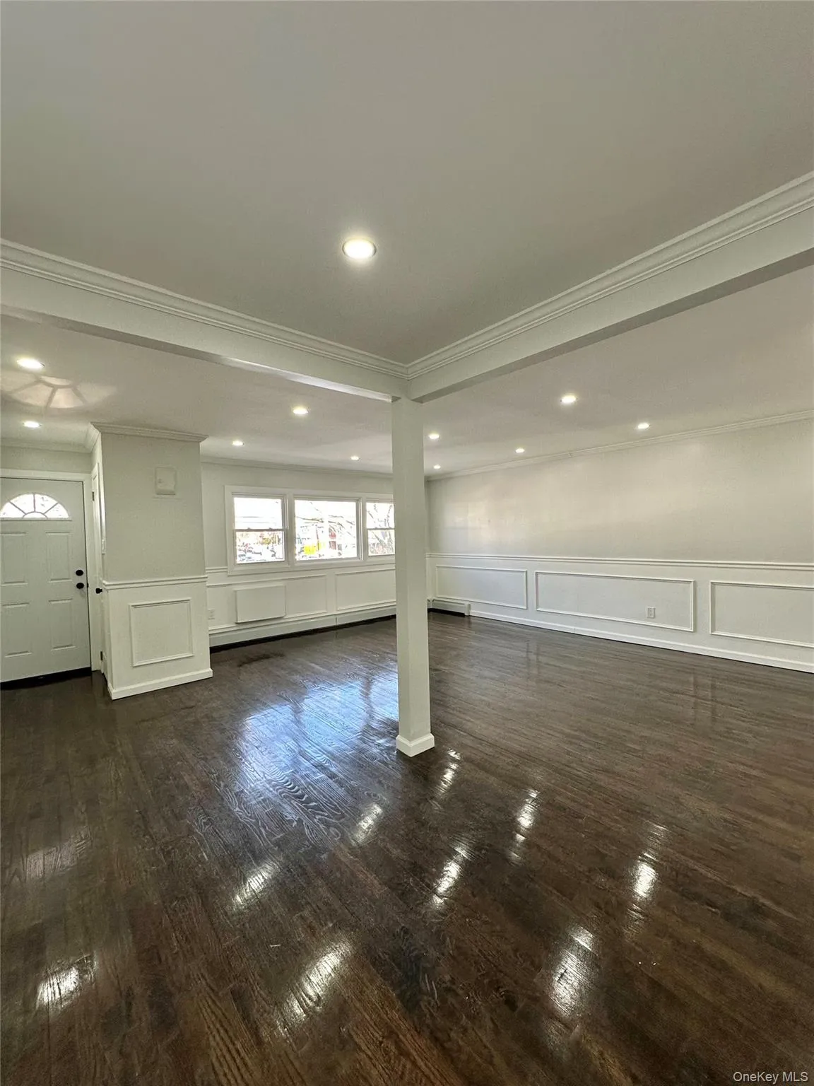 Unfurnished living room with a decorative wall, a wainscoted wall, dark wood finished floors, and crown molding Unfurnished living room with a decorative wall, a wainscoted wall, dark wood finished floors, and crown molding