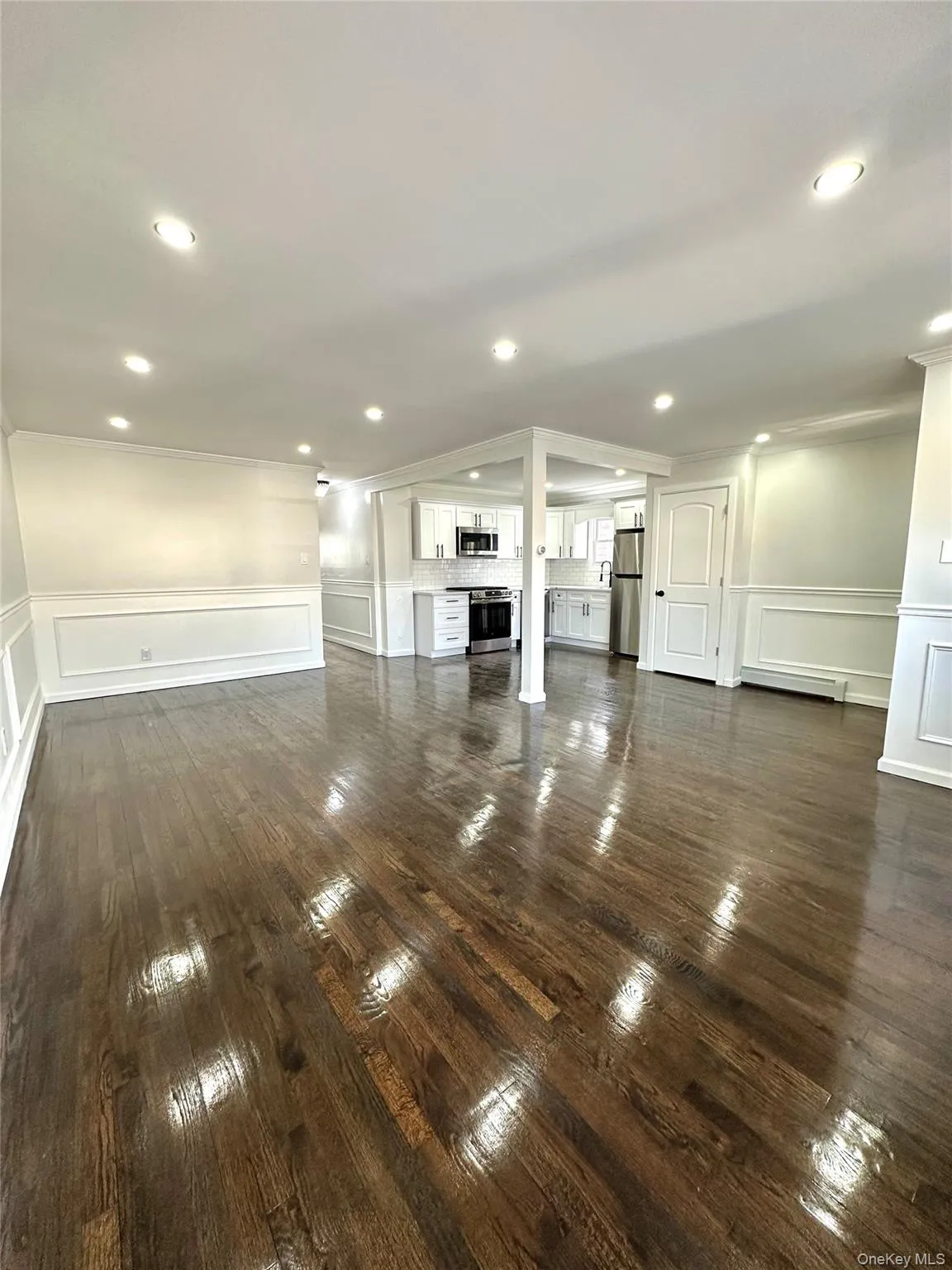 Unfurnished living room featuring a decorative wall, a wainscoted wall, recessed lighting, baseboard heating, and dark wood-style flooring Unfurnished living room featuring a decorative wall, a wainscoted wall, recessed lighting, baseboard heating, and dark wood-style flooring