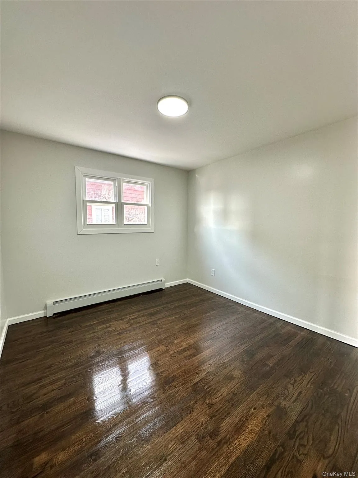 Empty room with baseboard heating and dark wood-style floors Empty room with baseboard heating and dark wood-style floors