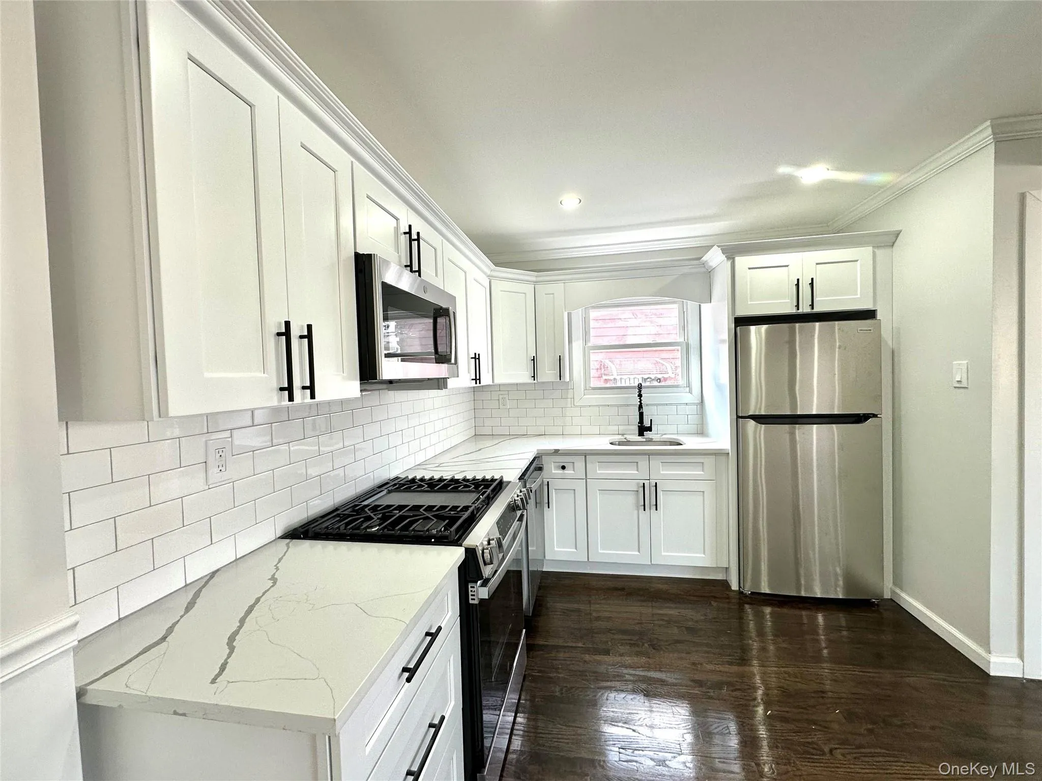 Kitchen with stainless steel appliances, white cabinets, light stone counters, decorative backsplash, and crown molding Kitchen with stainless steel appliances, white cabinets, light stone counters, decorative backsplash, and crown molding