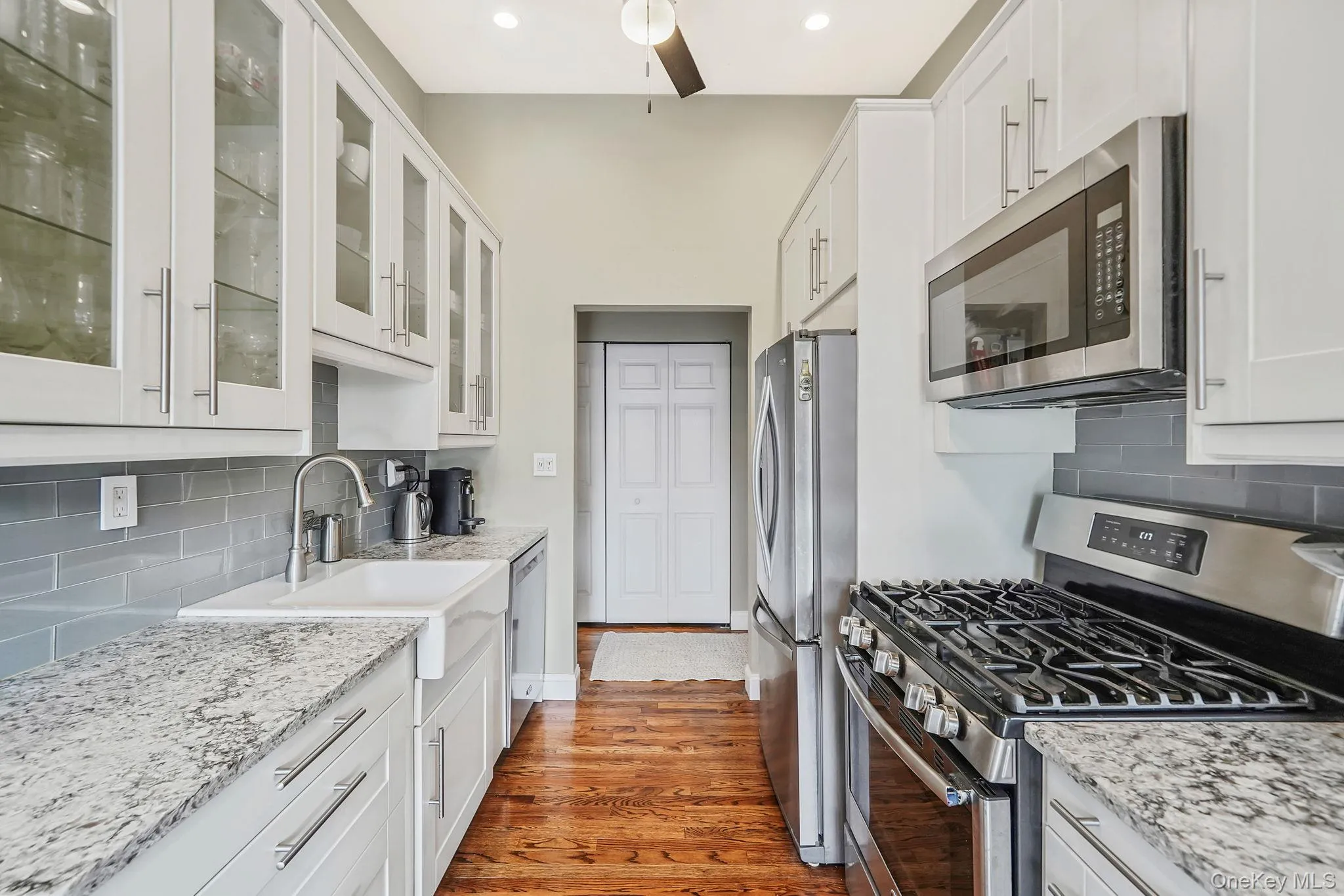Kitchen featuring decorative backsplash, stainless steel appliances, white cabinetry, and glass insert cabinets Kitchen featuring decorative backsplash, stainless steel appliances, white cabinetry, and glass insert cabinets