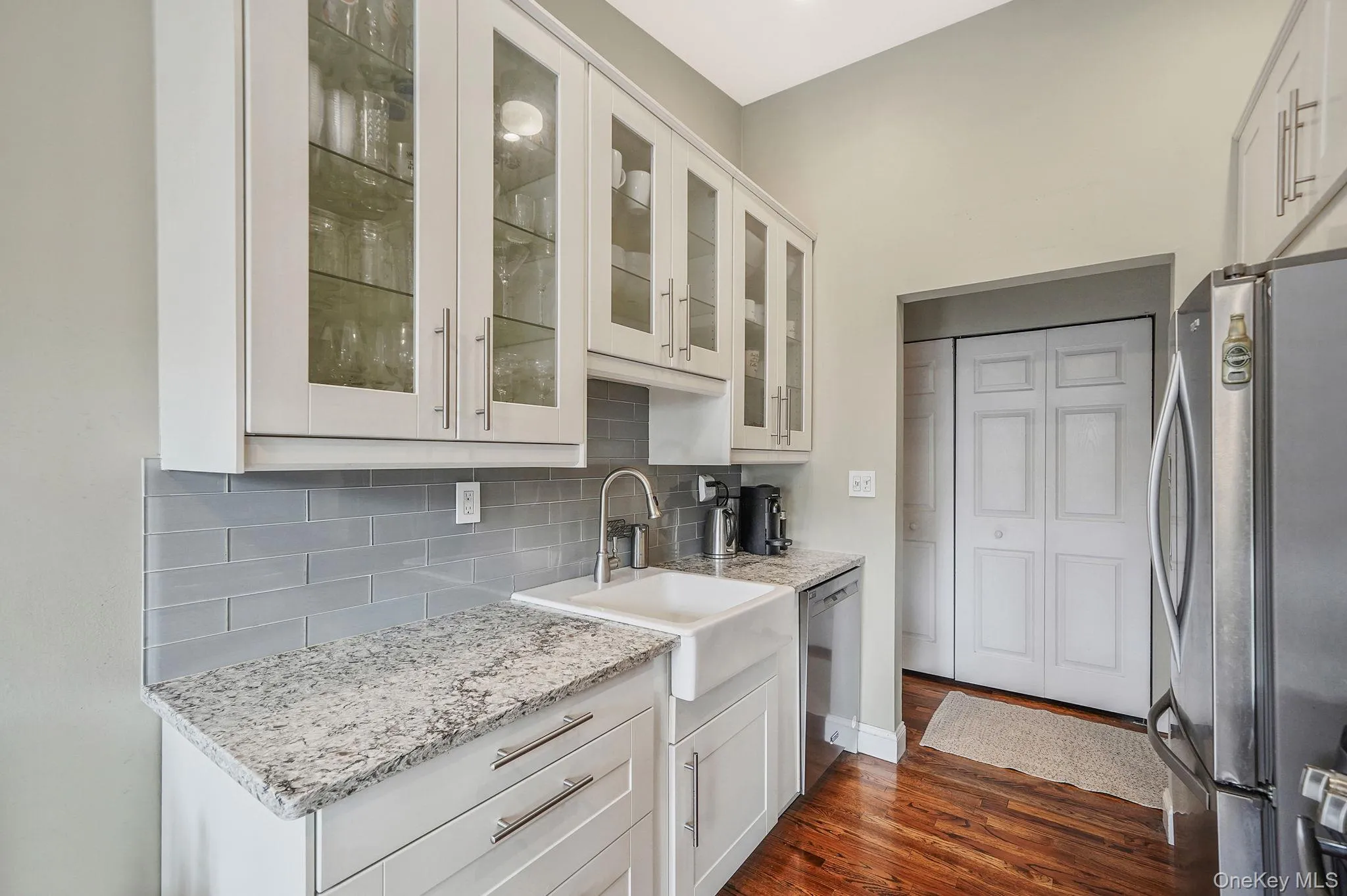Kitchen featuring appliances with stainless steel finishes, white cabinets, glass insert cabinets, light stone counters, and decorative backsplash Kitchen featuring appliances with stainless steel finishes, white cabinets, glass insert cabinets, light stone counters, and decorative backsplash
