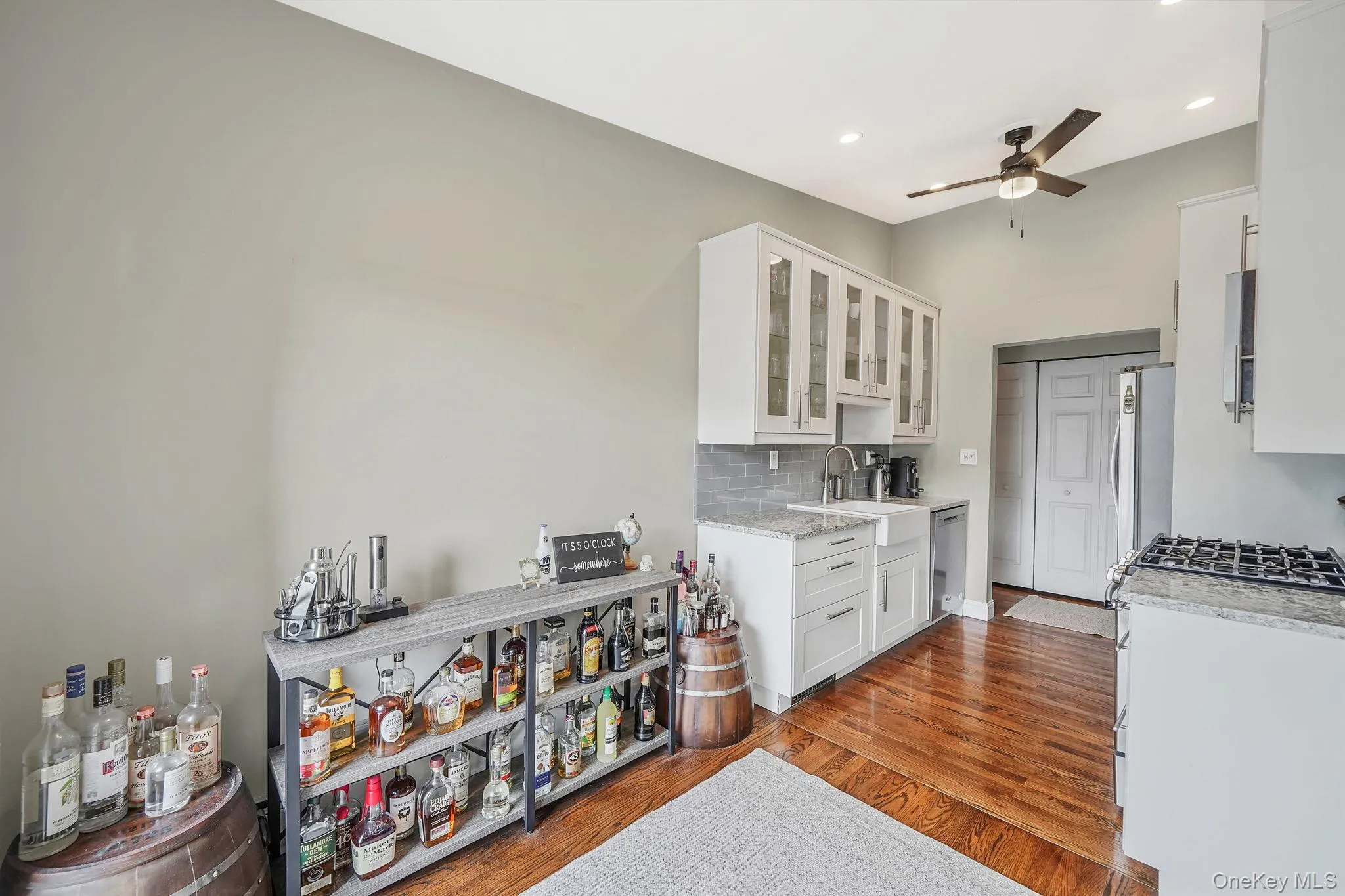 Kitchen featuring glass insert cabinets, white cabinetry, tasteful backsplash, light stone countertops, and light wood-style flooring Kitchen featuring glass insert cabinets, white cabinetry, tasteful backsplash, light stone countertops, and light wood-style flooring