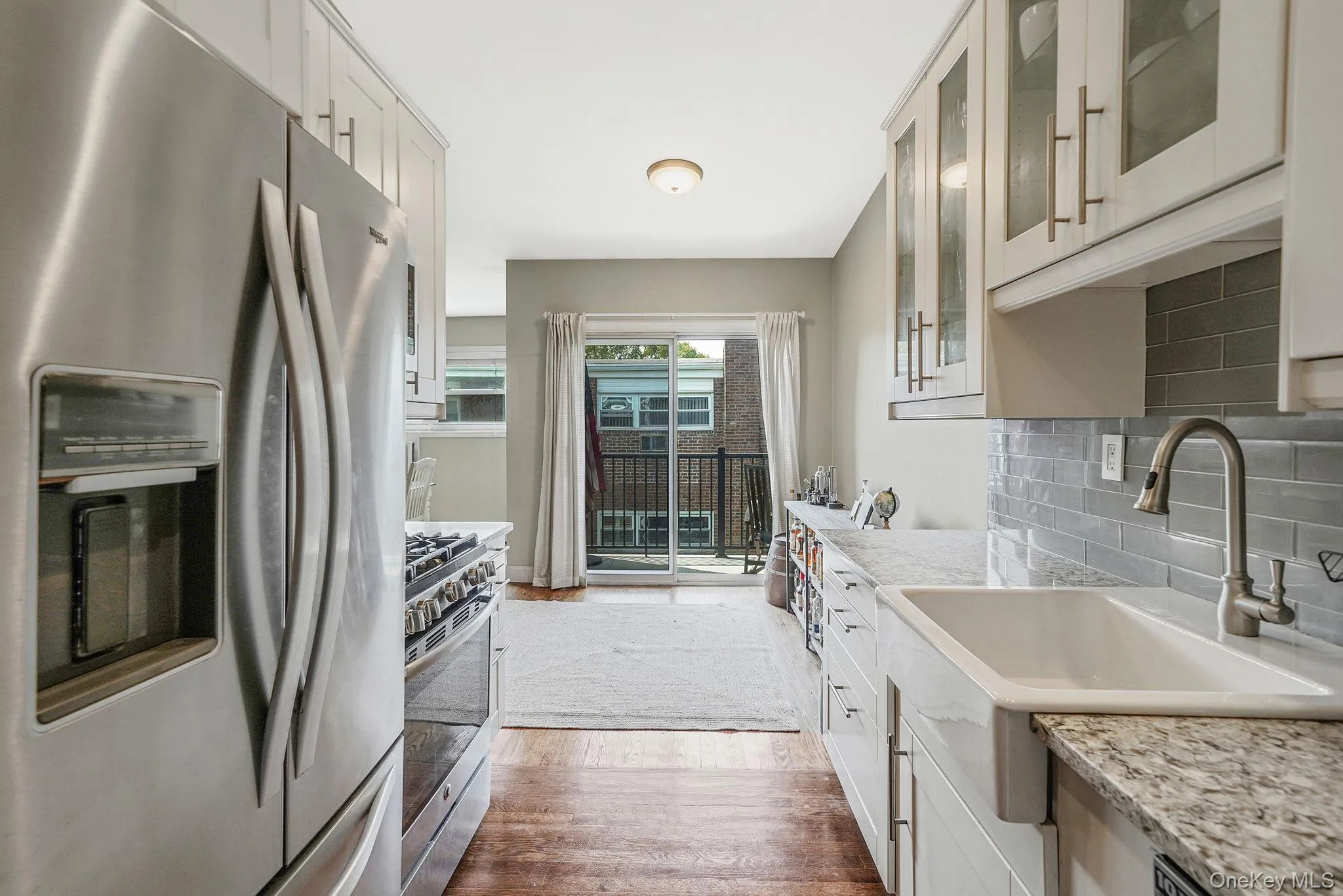 Kitchen with stainless steel appliances, decorative backsplash, glass insert cabinets, white cabinetry, and dark wood finished floors Kitchen with stainless steel appliances, decorative backsplash, glass insert cabinets, white cabinetry, and dark wood finished floors