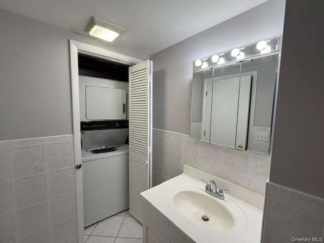 Bathroom featuring tile walls, stacked washer / dryer, vanity, a wainscoted wall, and light tile patterned floors Bathroom featuring tile walls, stacked washer / dryer, vanity, a wainscoted wall, and light tile patterned floors