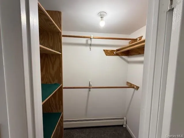 Spacious closet featuring a baseboard heating unit and dark colored carpet Spacious closet featuring a baseboard heating unit and dark colored carpet