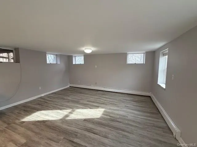 Basement featuring baseboard heating, light wood finished floors, healthy amount of natural light, and a baseboard radiator Basement featuring baseboard heating, light wood finished floors, healthy amount of natural light, and a baseboard radiator