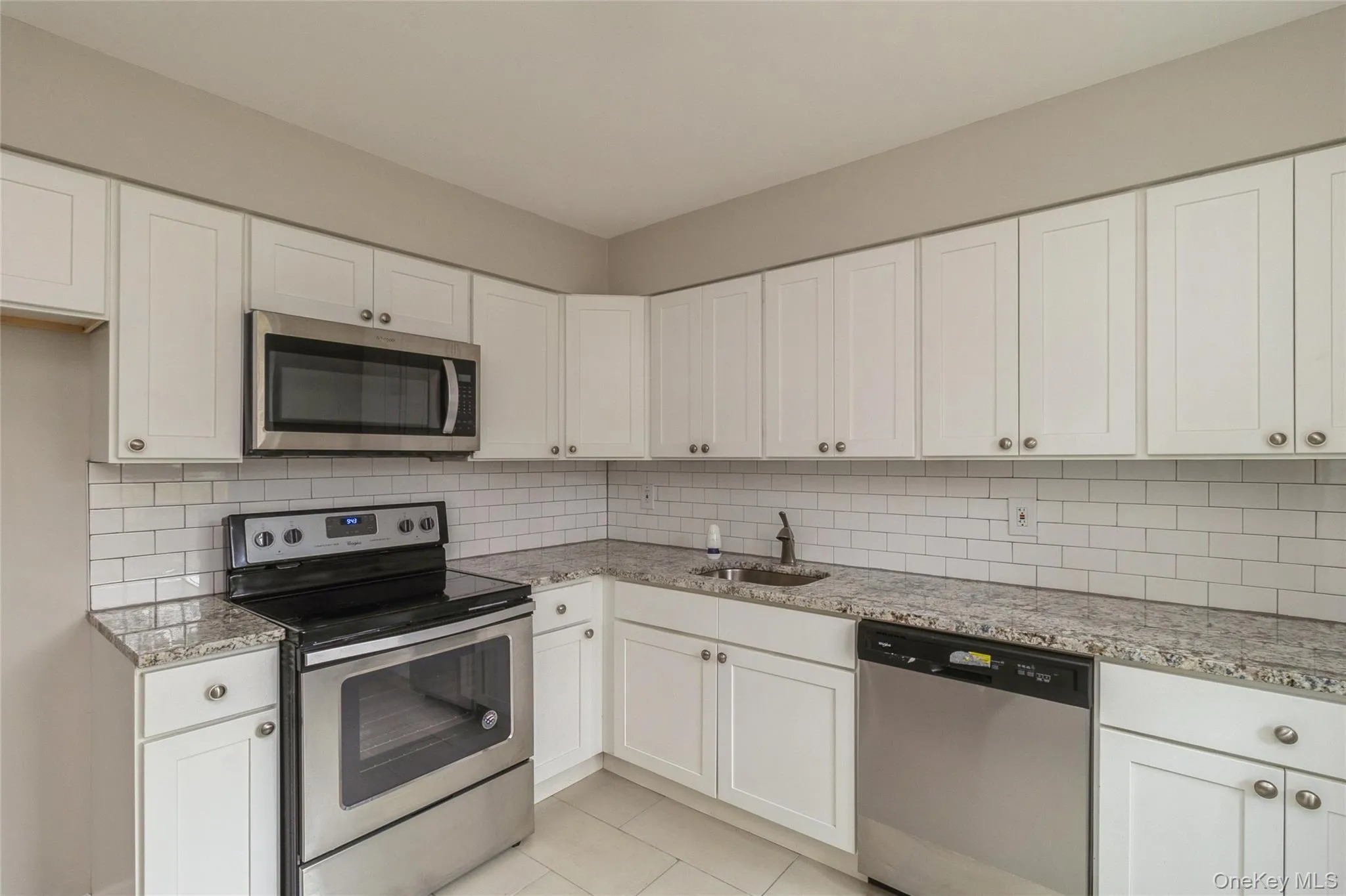 Kitchen featuring appliances with stainless steel finishes, white cabinetry, decorative backsplash, and light stone countertops Kitchen featuring appliances with stainless steel finishes, white cabinetry, decorative backsplash, and light stone countertops