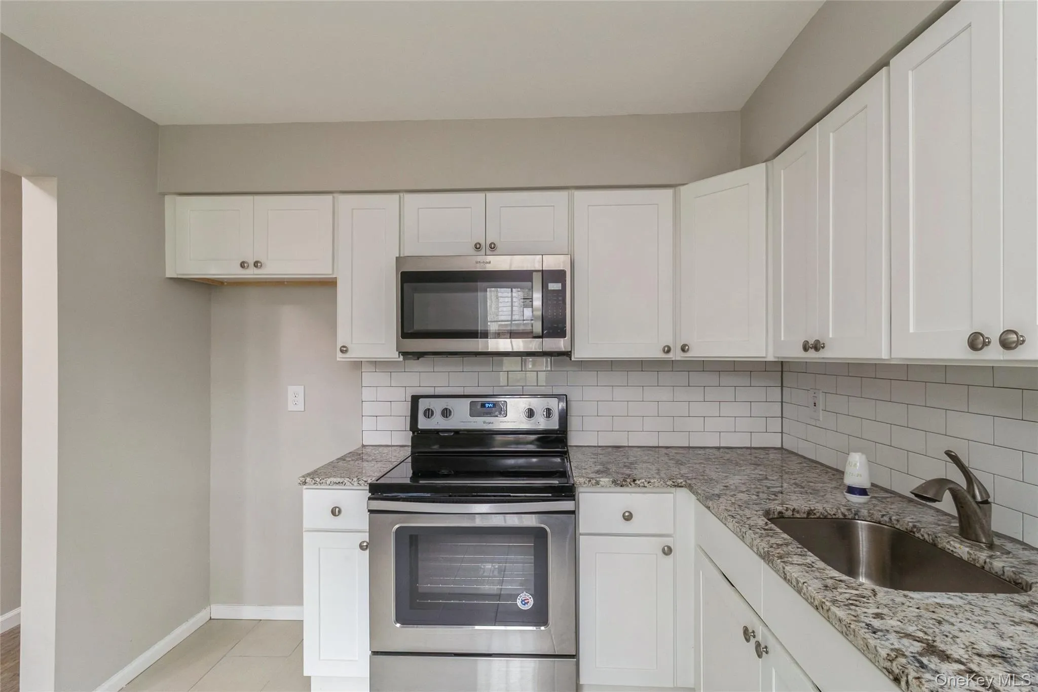 Kitchen with stainless steel appliances, light stone countertops, white cabinetry, and tasteful backsplash Kitchen with stainless steel appliances, light stone countertops, white cabinetry, and tasteful backsplash