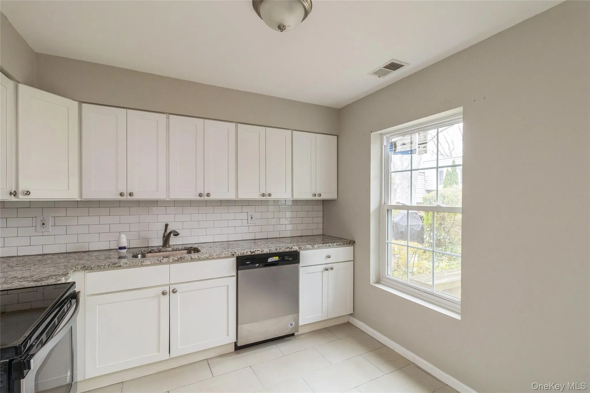 Kitchen featuring appliances with stainless steel finishes, white cabinetry, light stone countertops, light tile patterned floors, and backsplash Kitchen featuring appliances with stainless steel finishes, white cabinetry, light stone countertops, light tile patterned floors, and backsplash