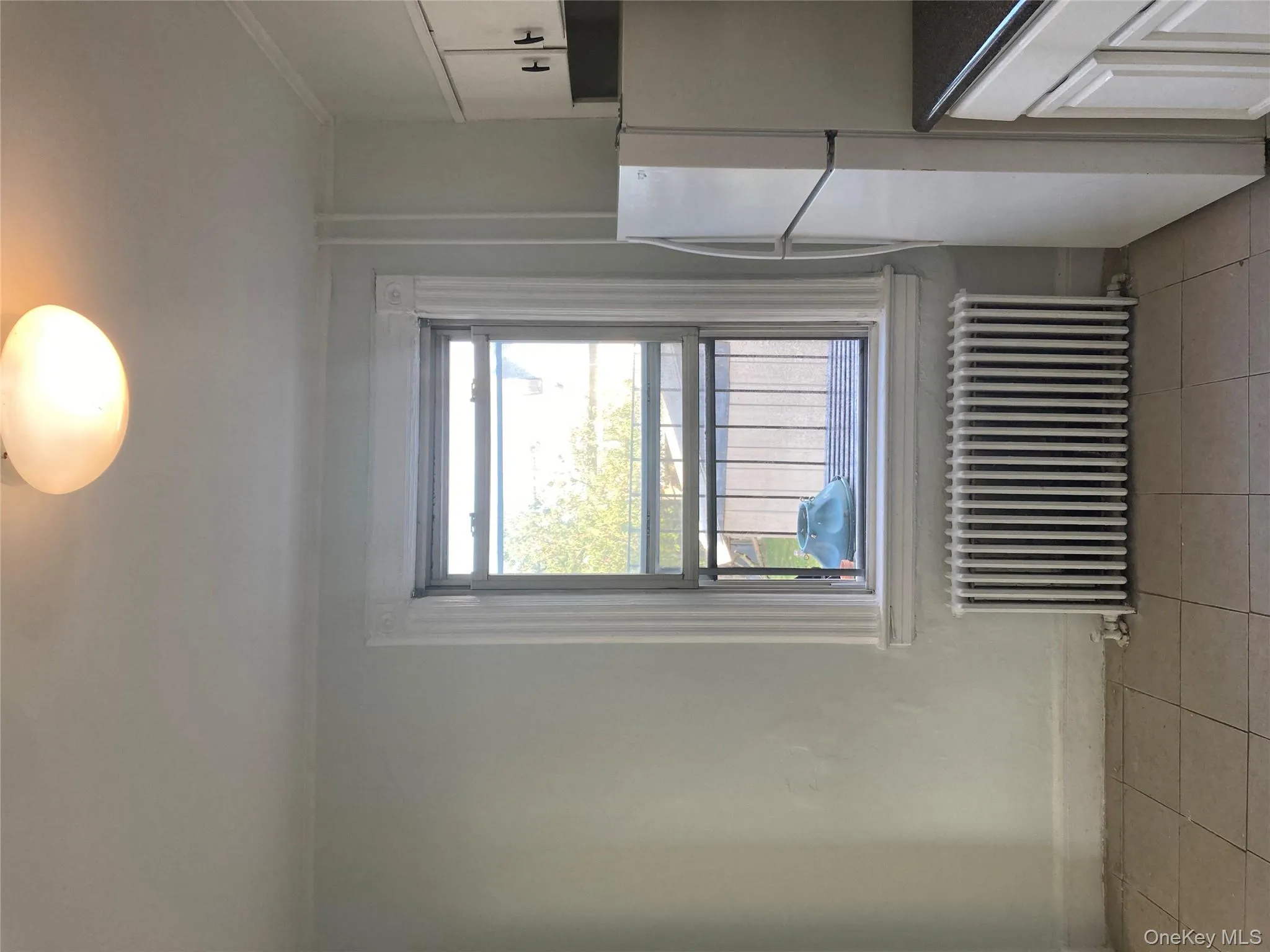 Kitchen featuring fridge, radiator and heating unit, light, tile patterned floors, white cabinets, and dark countertops. Fire Exit through Window. Kitchen featuring fridge, radiator and heating unit, light, tile patterned floors, white cabinets, and dark countertops. Fire Exit through Window.