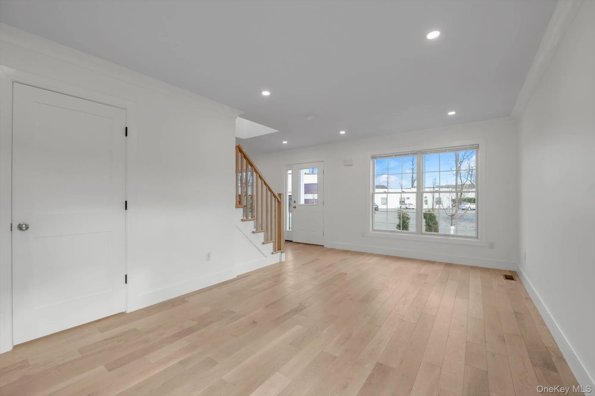 Unfurnished living room with light wood-type flooring, stairs, recessed lighting, and ornamental molding Unfurnished living room with light wood-type flooring, stairs, recessed lighting, and ornamental molding