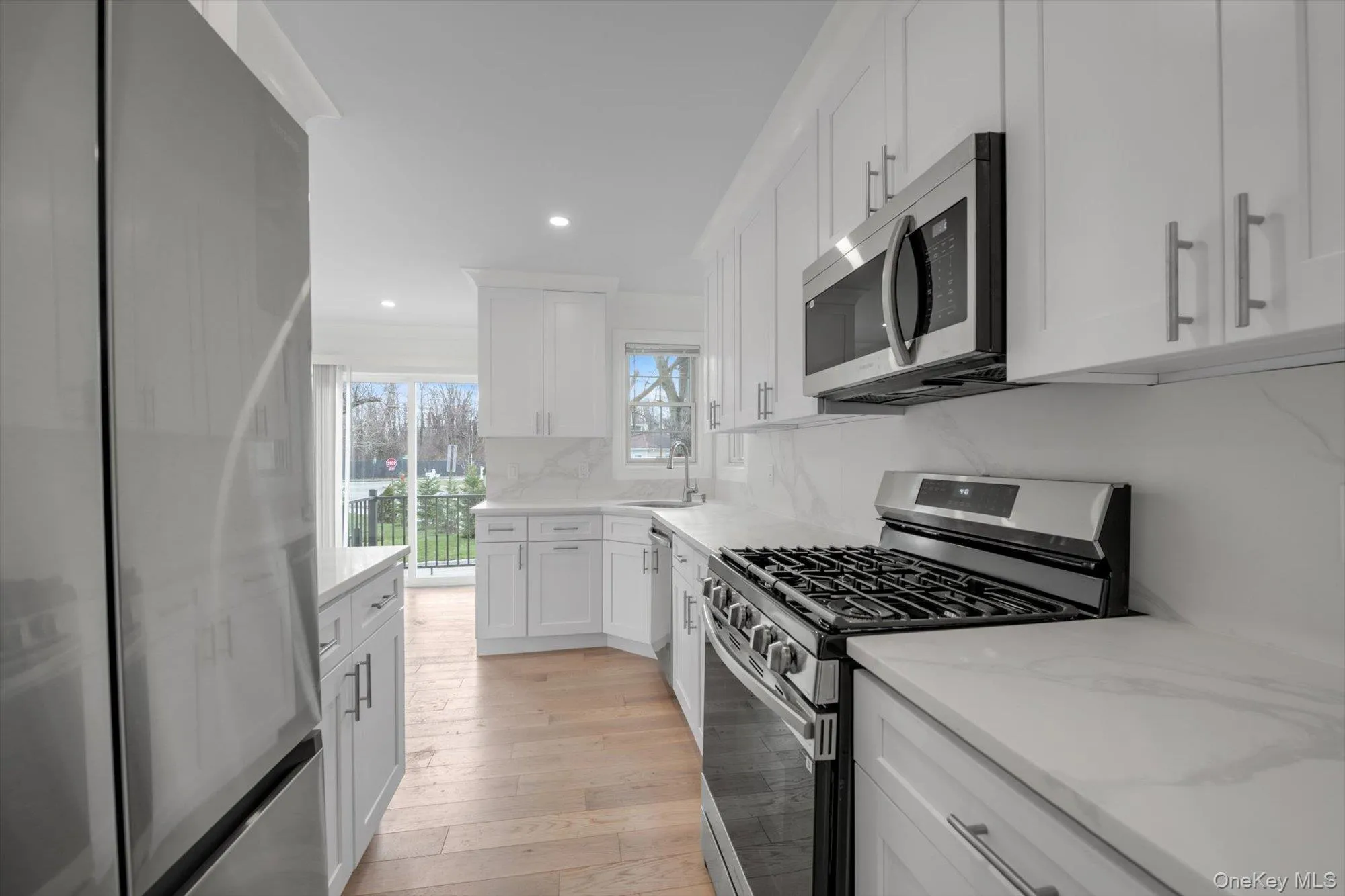 Kitchen featuring appliances with stainless steel finishes, white cabinets, light wood-style floors, light stone countertops, and recessed lighting Kitchen featuring appliances with stainless steel finishes, white cabinets, light wood-style floors, light stone countertops, and recessed lighting
