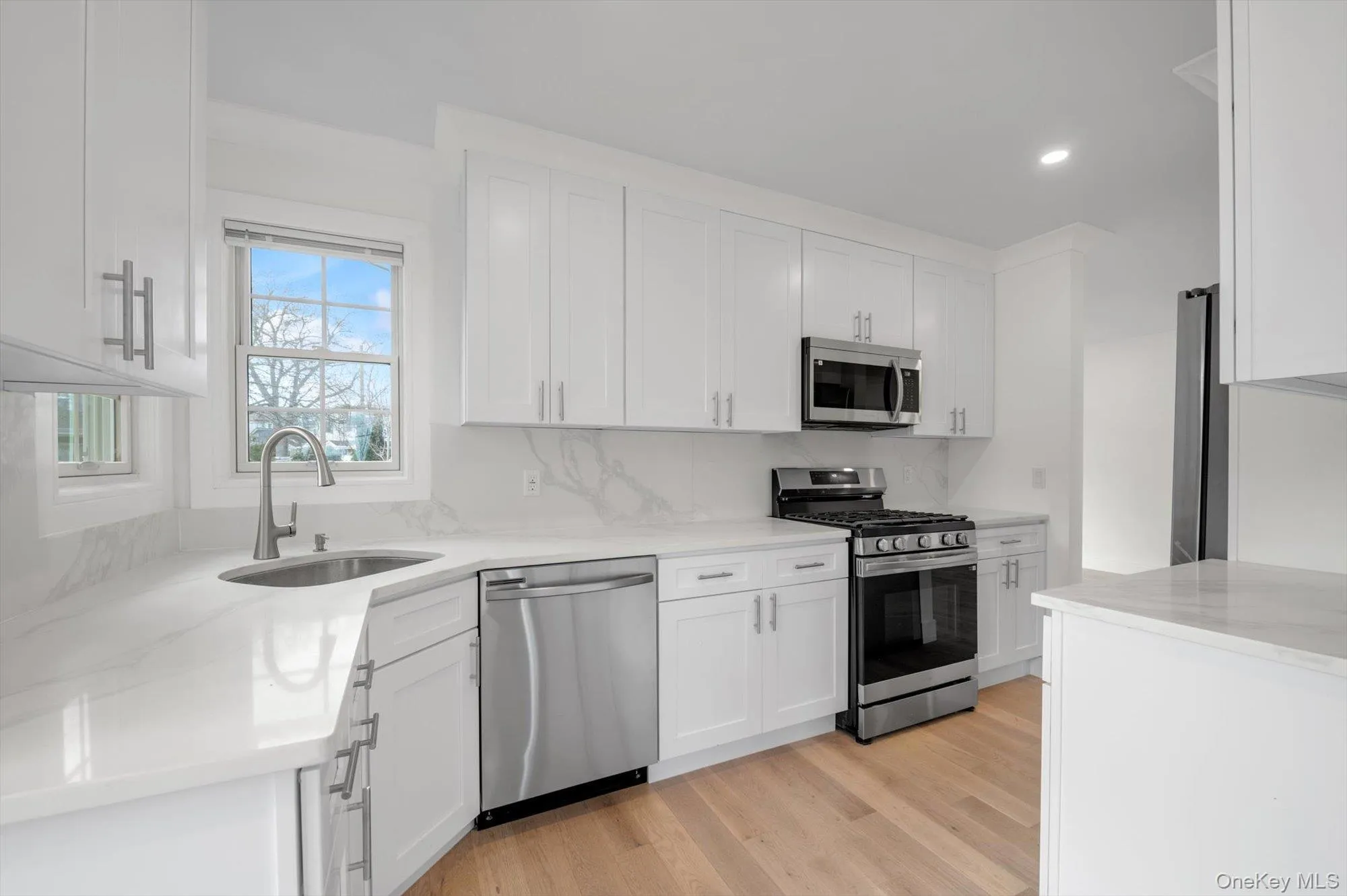 Kitchen with appliances with stainless steel finishes, light wood-type flooring, white cabinets, light stone counters, and decorative backsplash Kitchen with appliances with stainless steel finishes, light wood-type flooring, white cabinets, light stone counters, and decorative backsplash