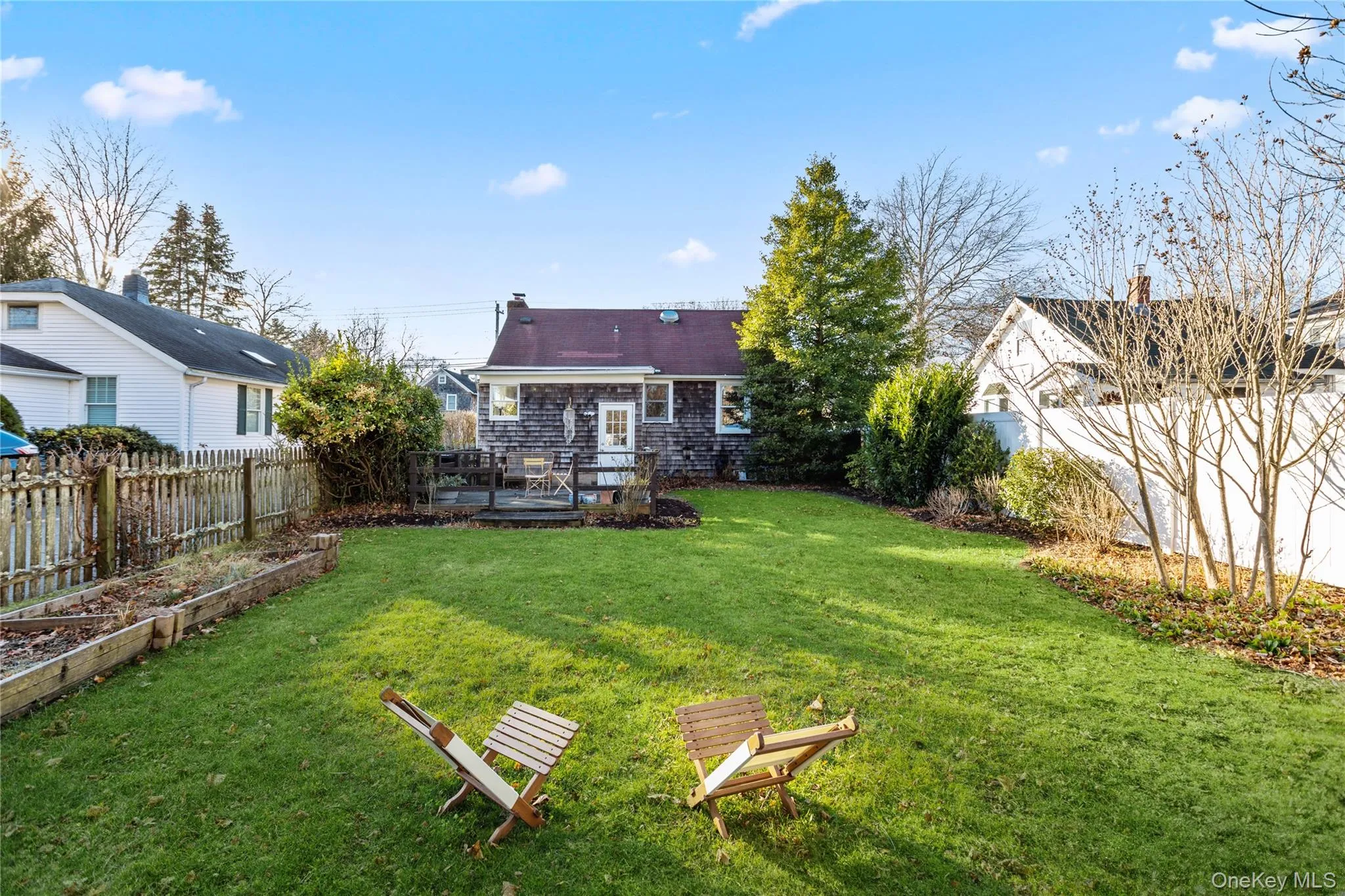 Rear view of house featuring a fenced backyard, a wooden deck, a garden, and a chimney Rear view of house featuring a fenced backyard, a wooden deck, a garden, and a chimney