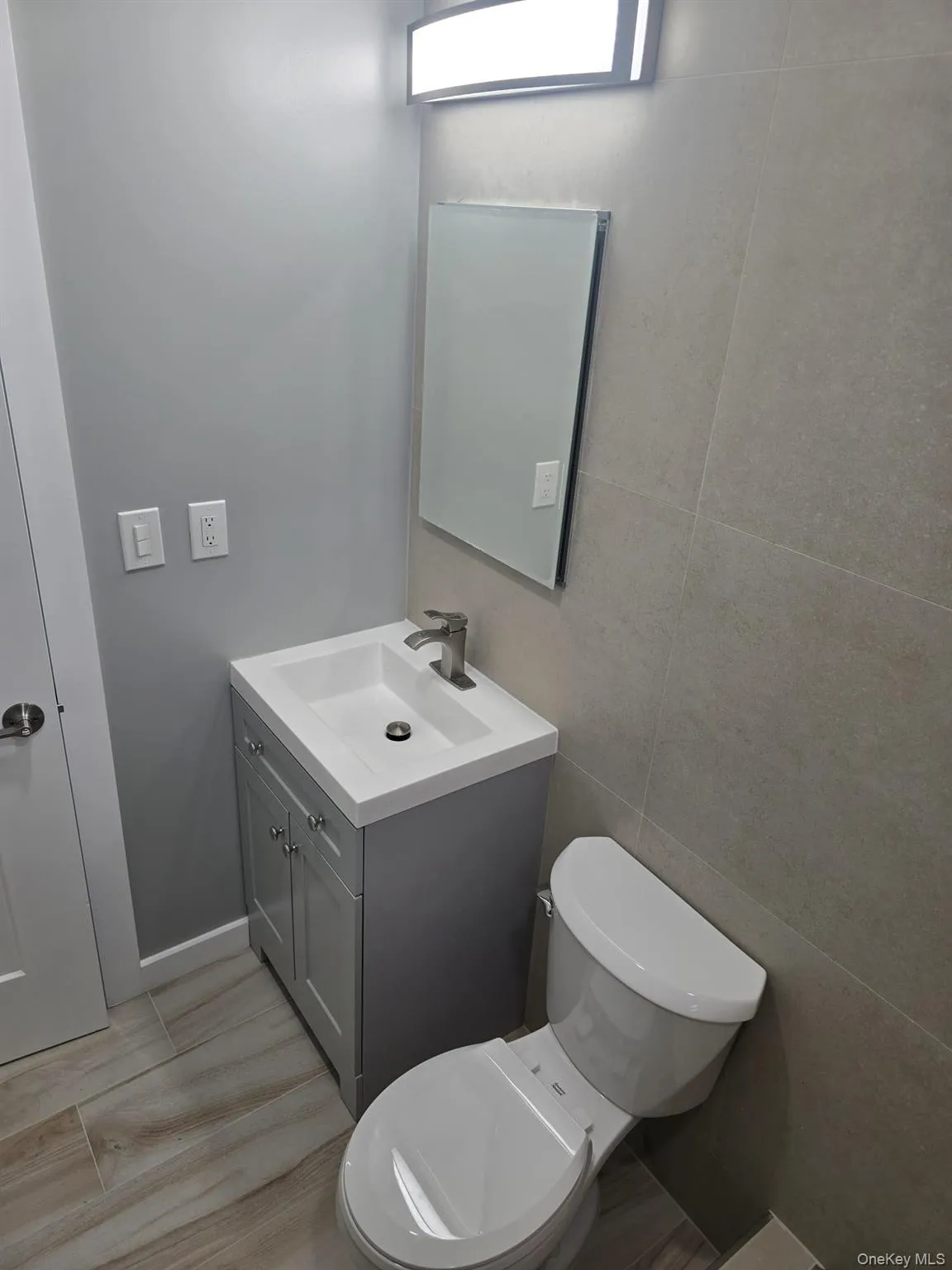 Half bath featuring tile walls, vanity, and wood finish floors Half bath featuring tile walls, vanity, and wood finish floors