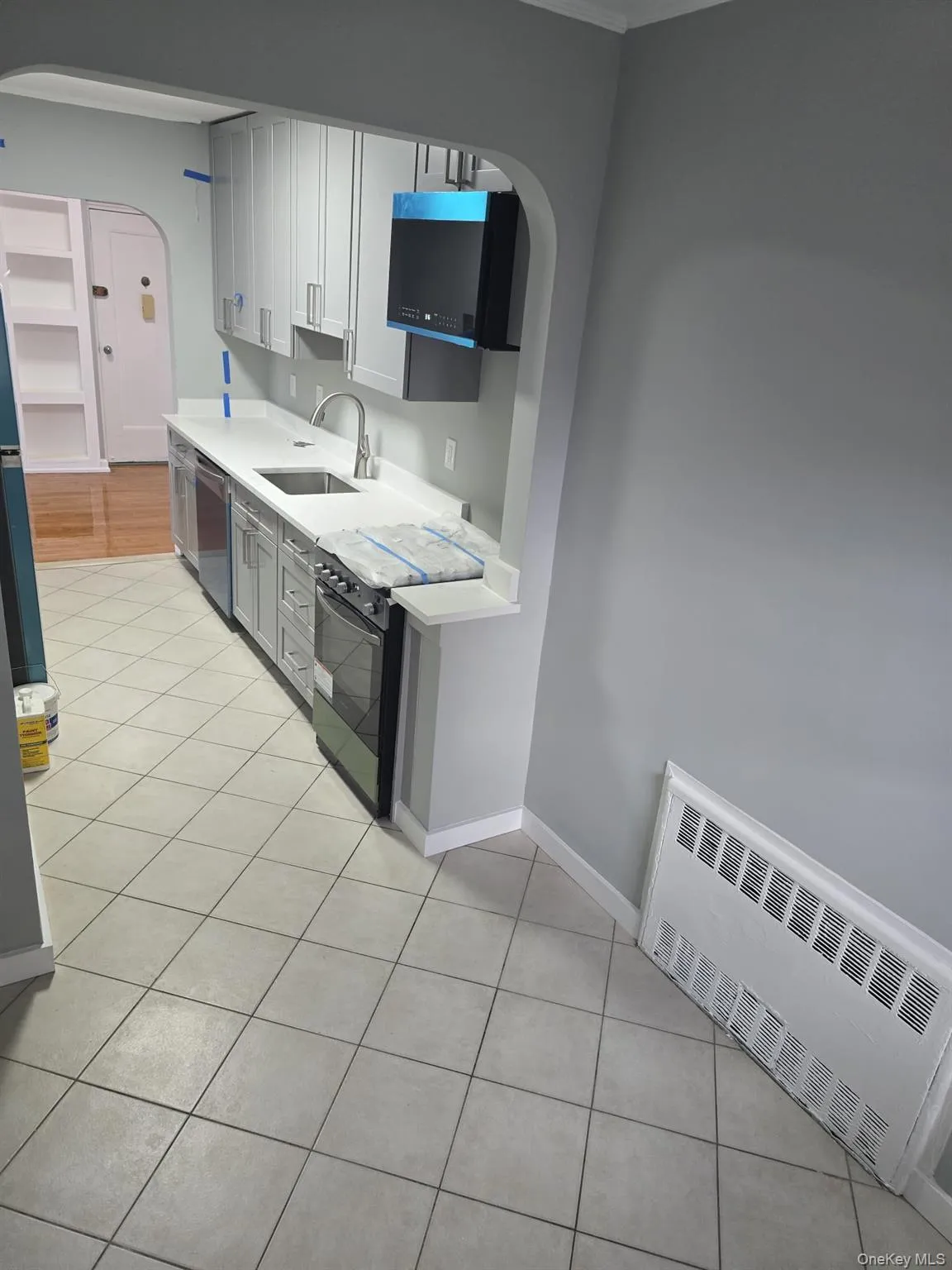 Kitchen featuring arched walkways, radiator heating unit, range with electric cooktop, light tile patterned floors, and dishwasher Kitchen featuring arched walkways, radiator heating unit, range with electric cooktop, light tile patterned floors, and dishwasher