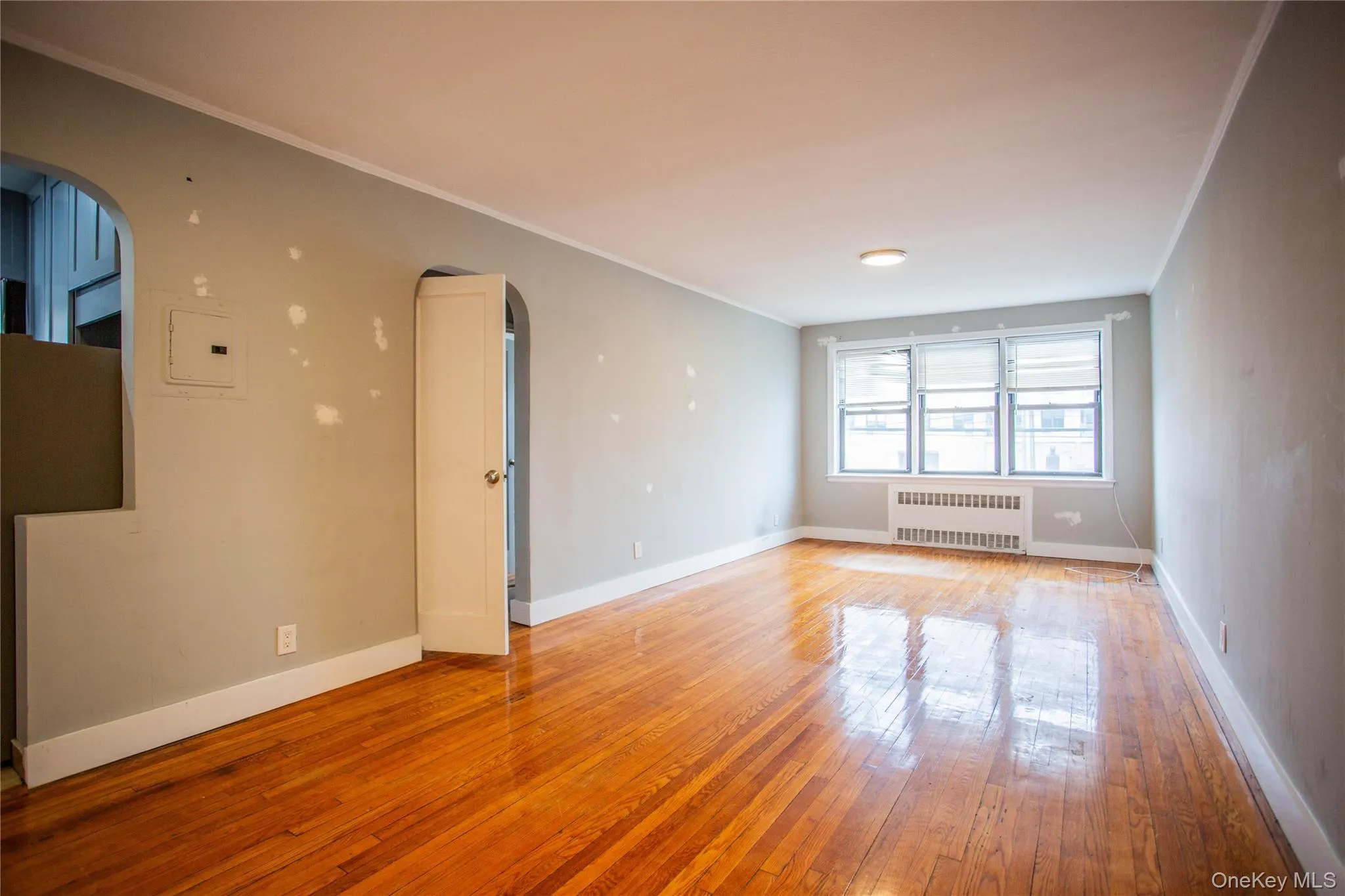 Empty room with arched walkways, radiator, light wood-style floors, and baseboards Empty room with arched walkways, radiator, light wood-style floors, and baseboards