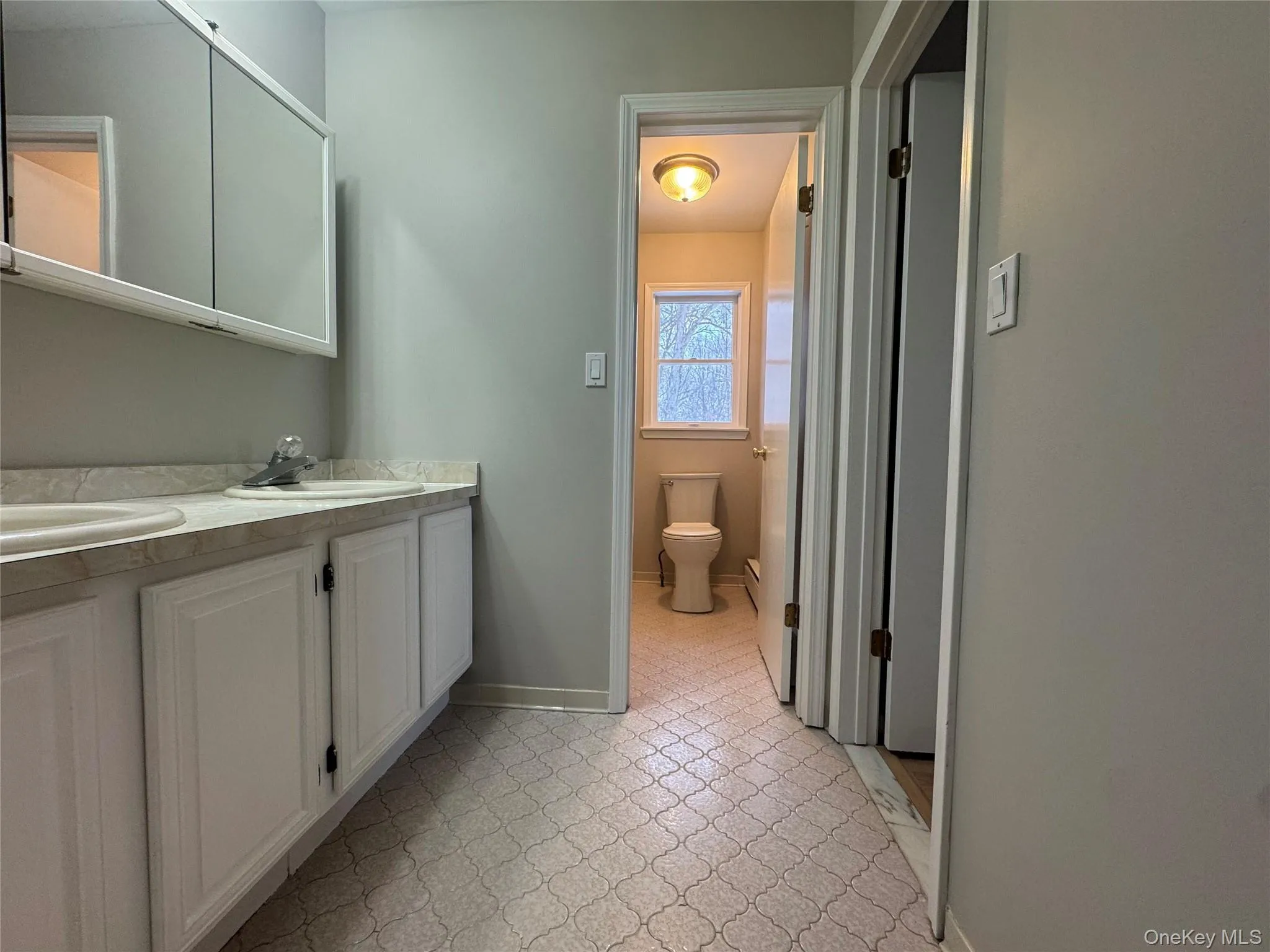 Full bath featuring double vanity, light flooring, and a baseboard radiator Full bath featuring double vanity, light flooring, and a baseboard radiator