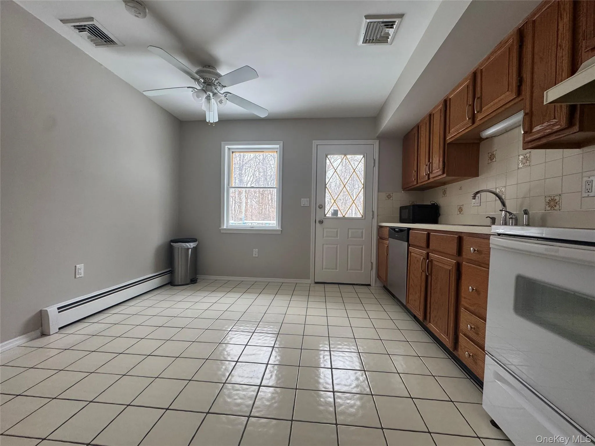 Kitchen featuring white range with electric cooktop, brown cabinets, light countertops, baseboard heating, and backsplash Kitchen featuring white range with electric cooktop, brown cabinets, light countertops, baseboard heating, and backsplash