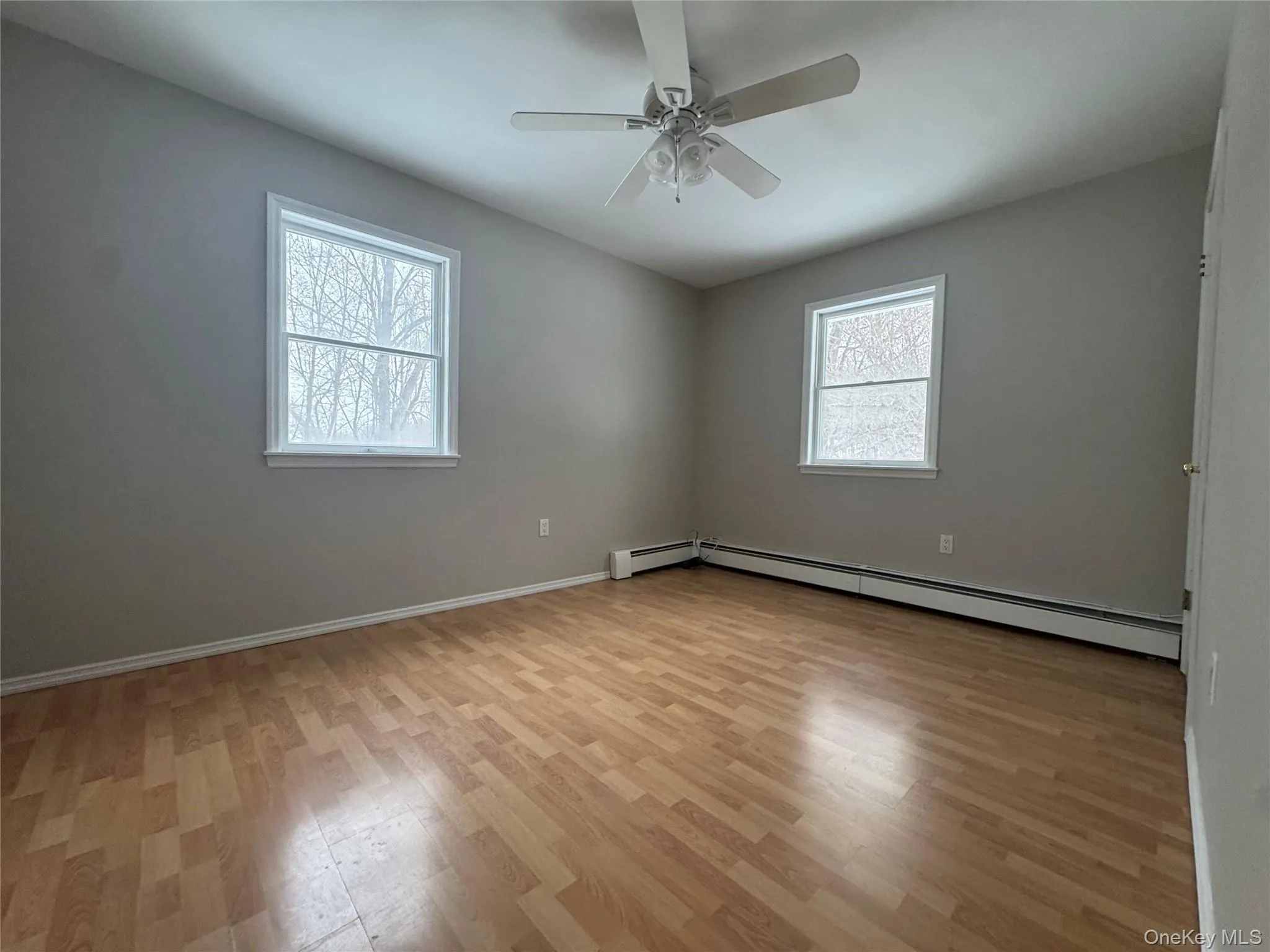 Empty room with light wood-type flooring, a baseboard heating unit, plenty of natural light, and ceiling fan Empty room with light wood-type flooring, a baseboard heating unit, plenty of natural light, and ceiling fan