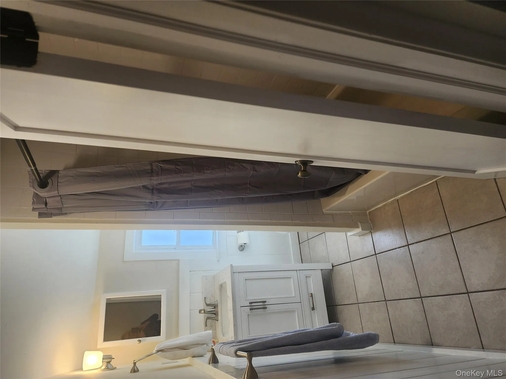 Full bathroom featuring light tile patterned flooring, vanity, shower / bath combo, and wainscoting Full bathroom featuring light tile patterned flooring, vanity, shower / bath combo, and wainscoting