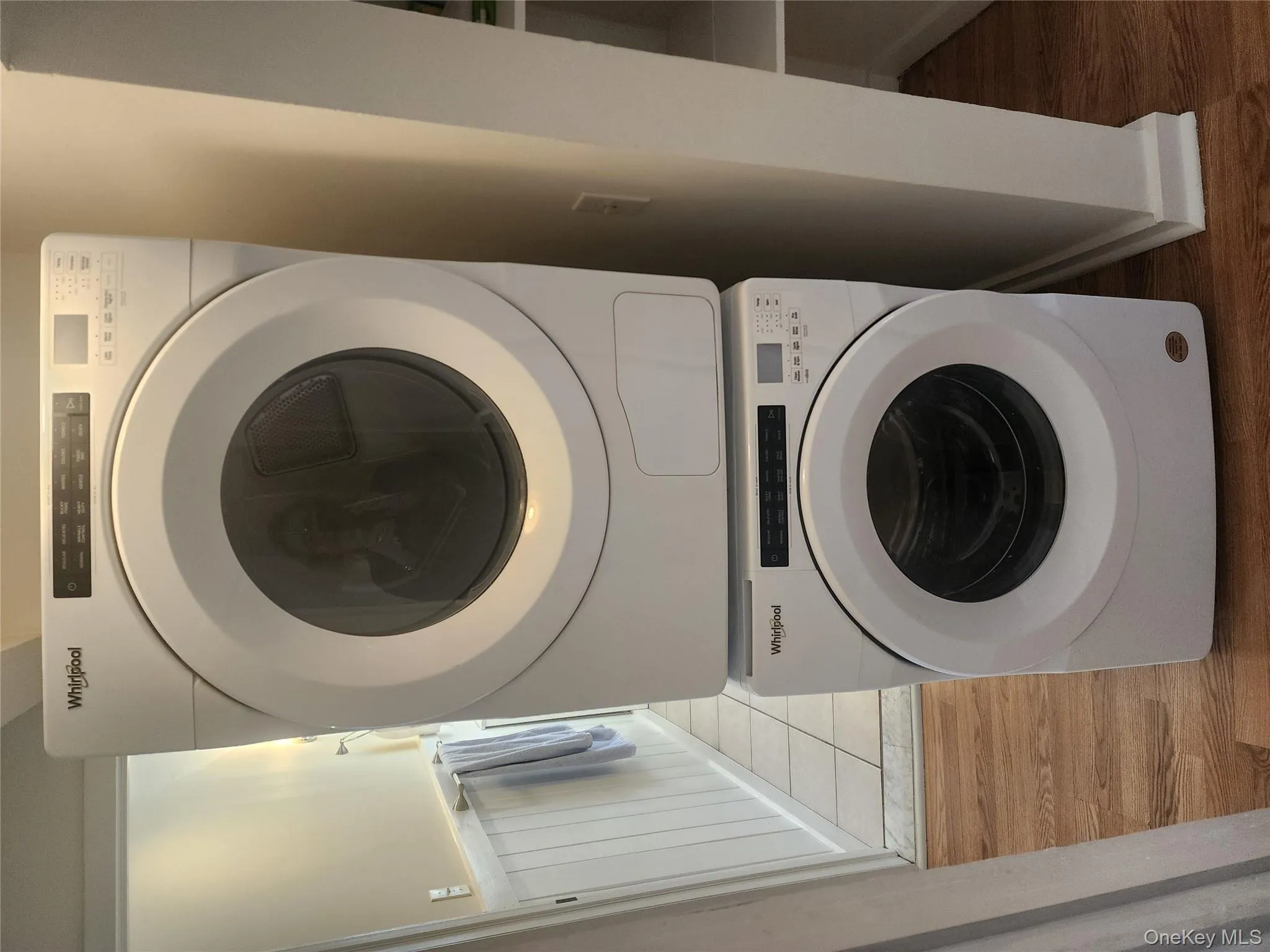 Laundry room featuring light wood-style floors, stacked washer and clothes dryer, and a wainscoted wall Laundry room featuring light wood-style floors, stacked washer and clothes dryer, and a wainscoted wall