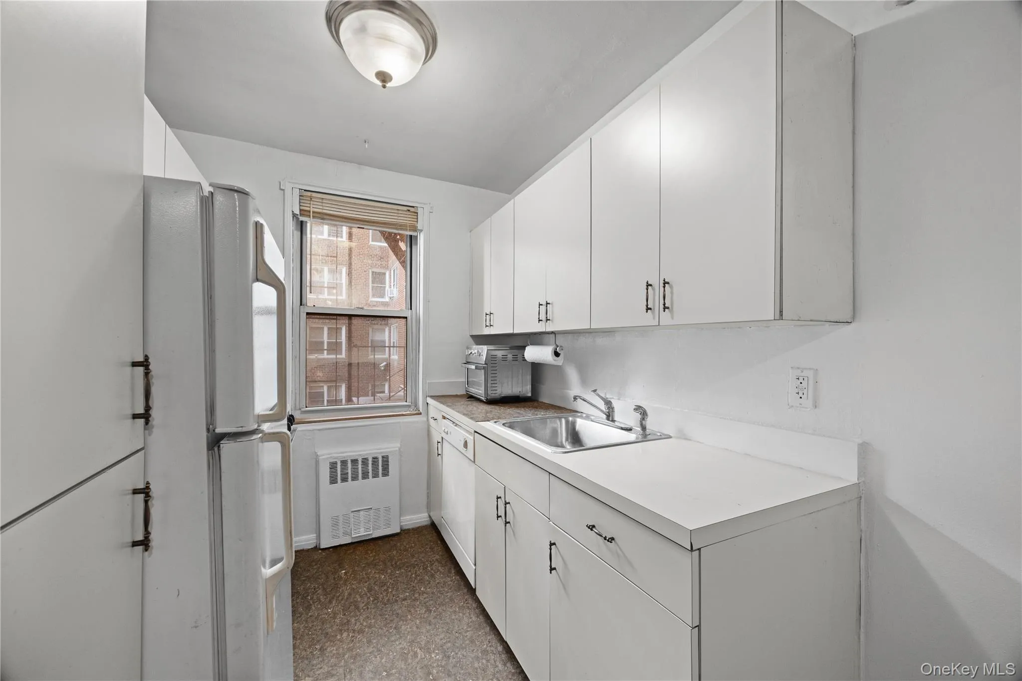 Kitchen featuring light countertops, white appliances, white cabinetry, radiator, and dark flooring Kitchen featuring light countertops, white appliances, white cabinetry, radiator, and dark flooring
