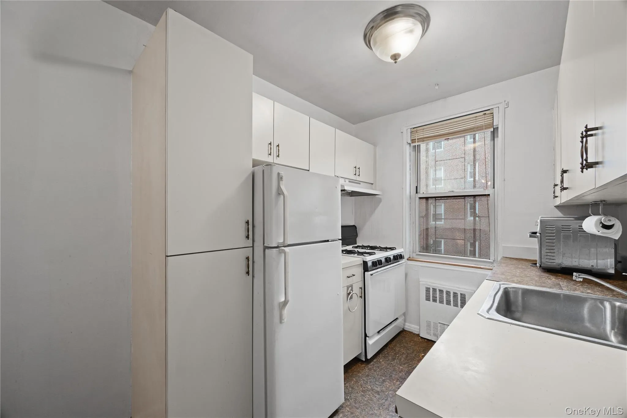 Kitchen with white appliances, light countertops, white cabinetry, and radiator heating unit Kitchen with white appliances, light countertops, white cabinetry, and radiator heating unit
