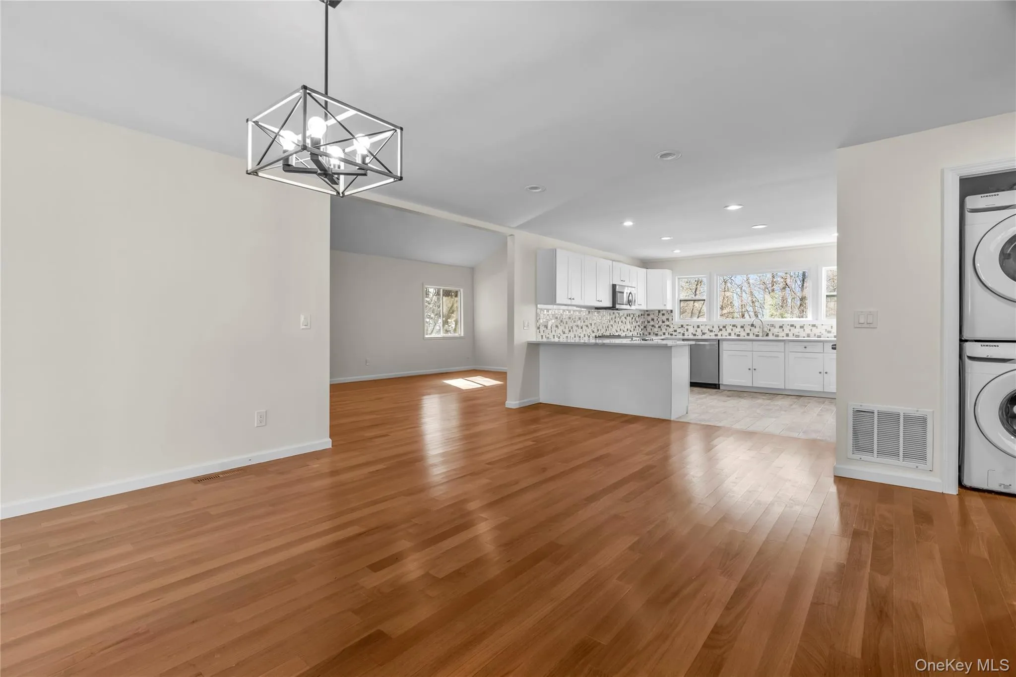 Unfurnished living room with stacked washer / dryer, an inviting chandelier, and light wood-type flooring Unfurnished living room with stacked washer / dryer, an inviting chandelier, and light wood-type flooring