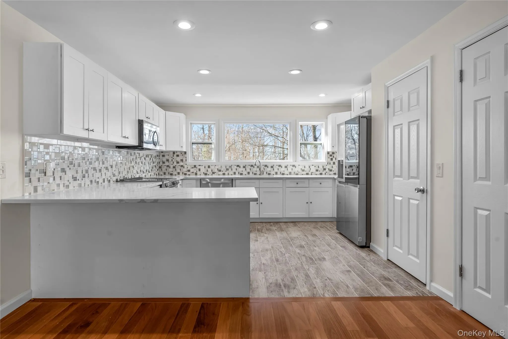 Kitchen with white cabinetry, kitchen peninsula, light wood-type flooring, stainless steel appliances, and backsplash Kitchen with white cabinetry, kitchen peninsula, light wood-type flooring, stainless steel appliances, and backsplash