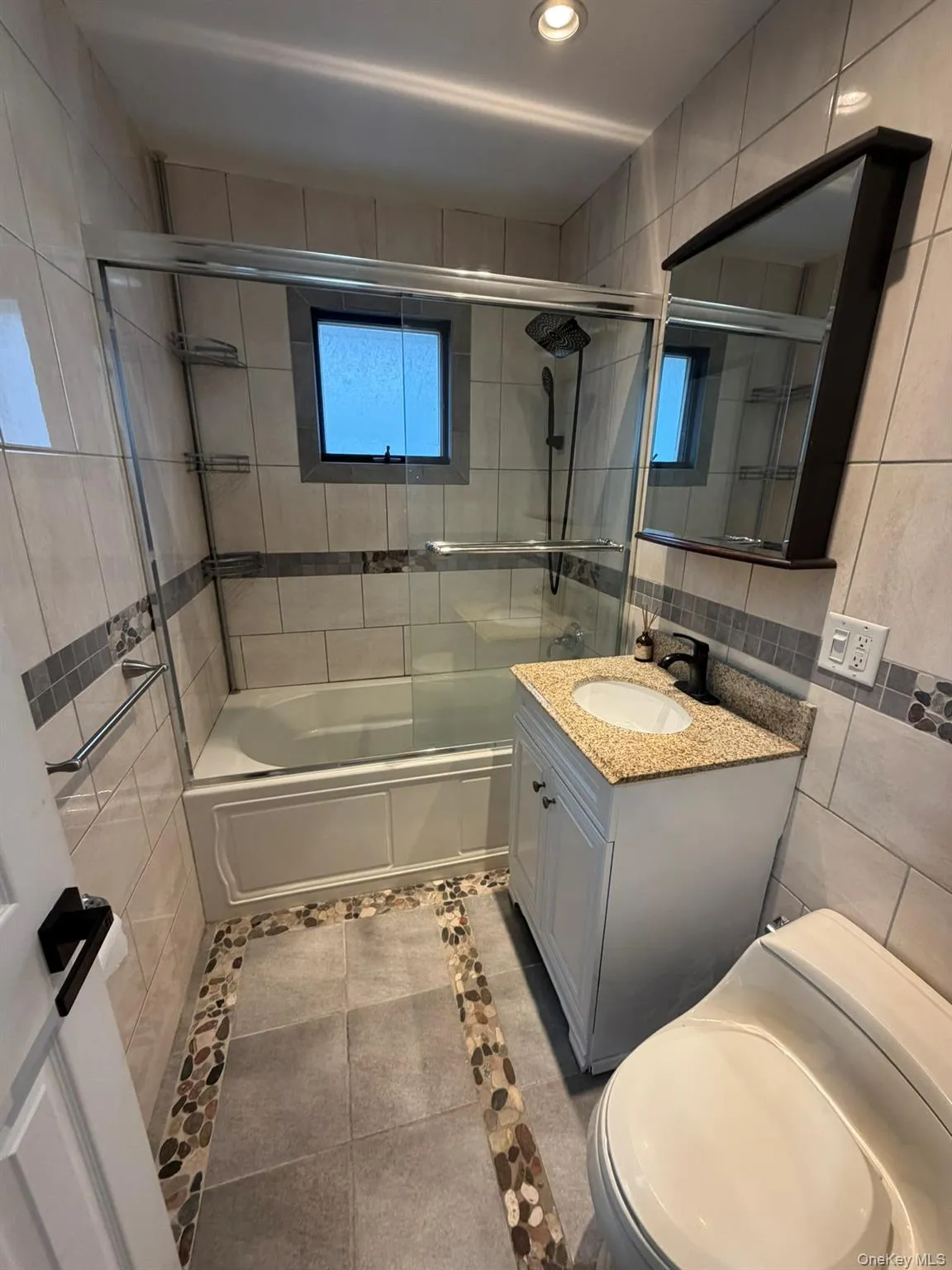 Bathroom with tile walls, vanity, combined bath / shower with glass door, light tile patterned floors, and recessed lighting Bathroom with tile walls, vanity, combined bath / shower with glass door, light tile patterned floors, and recessed lighting