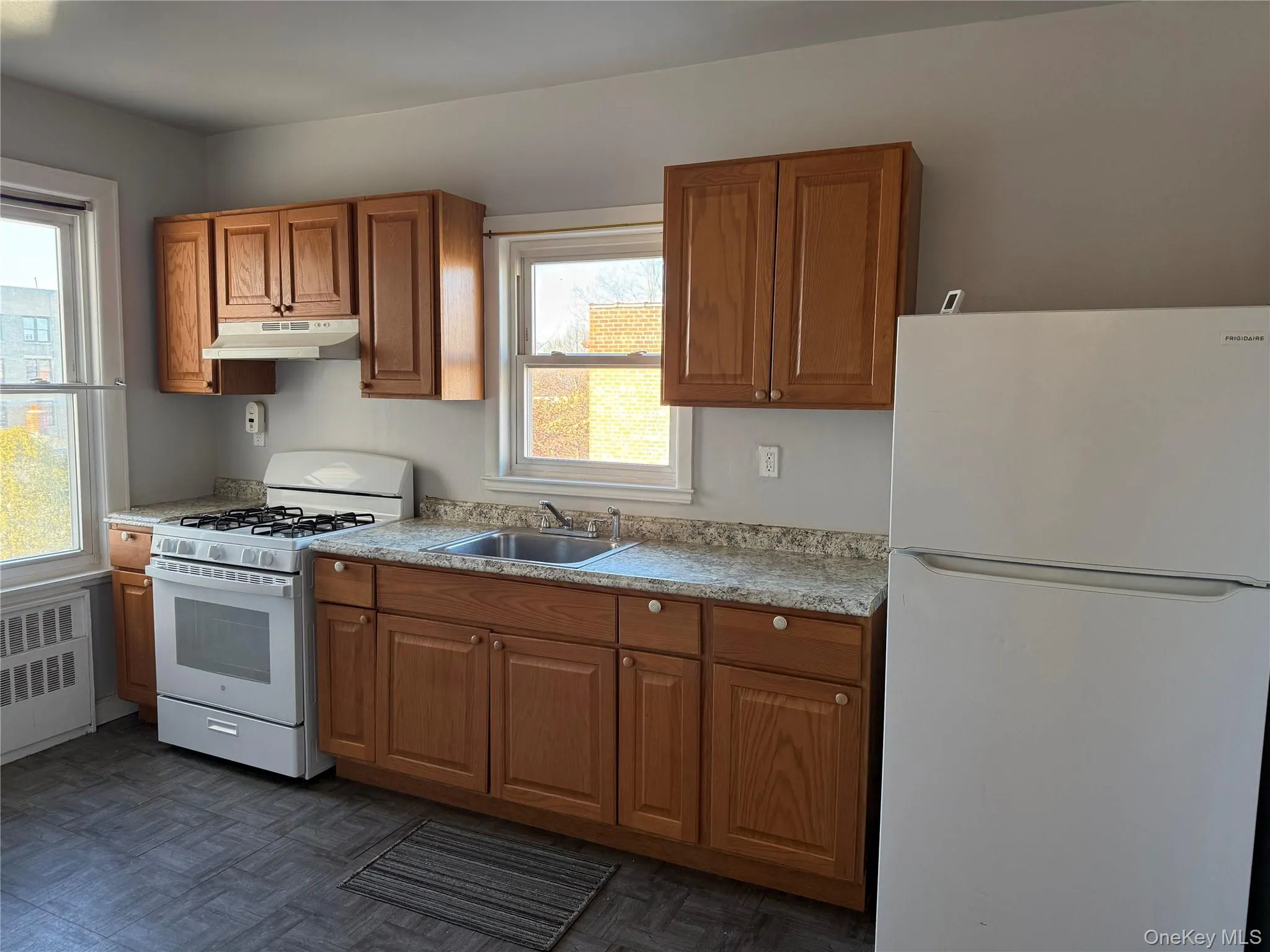 Kitchen featuring white appliances, brown cabinets, light countertops, and under cabinet range hood Kitchen featuring white appliances, brown cabinets, light countertops, and under cabinet range hood