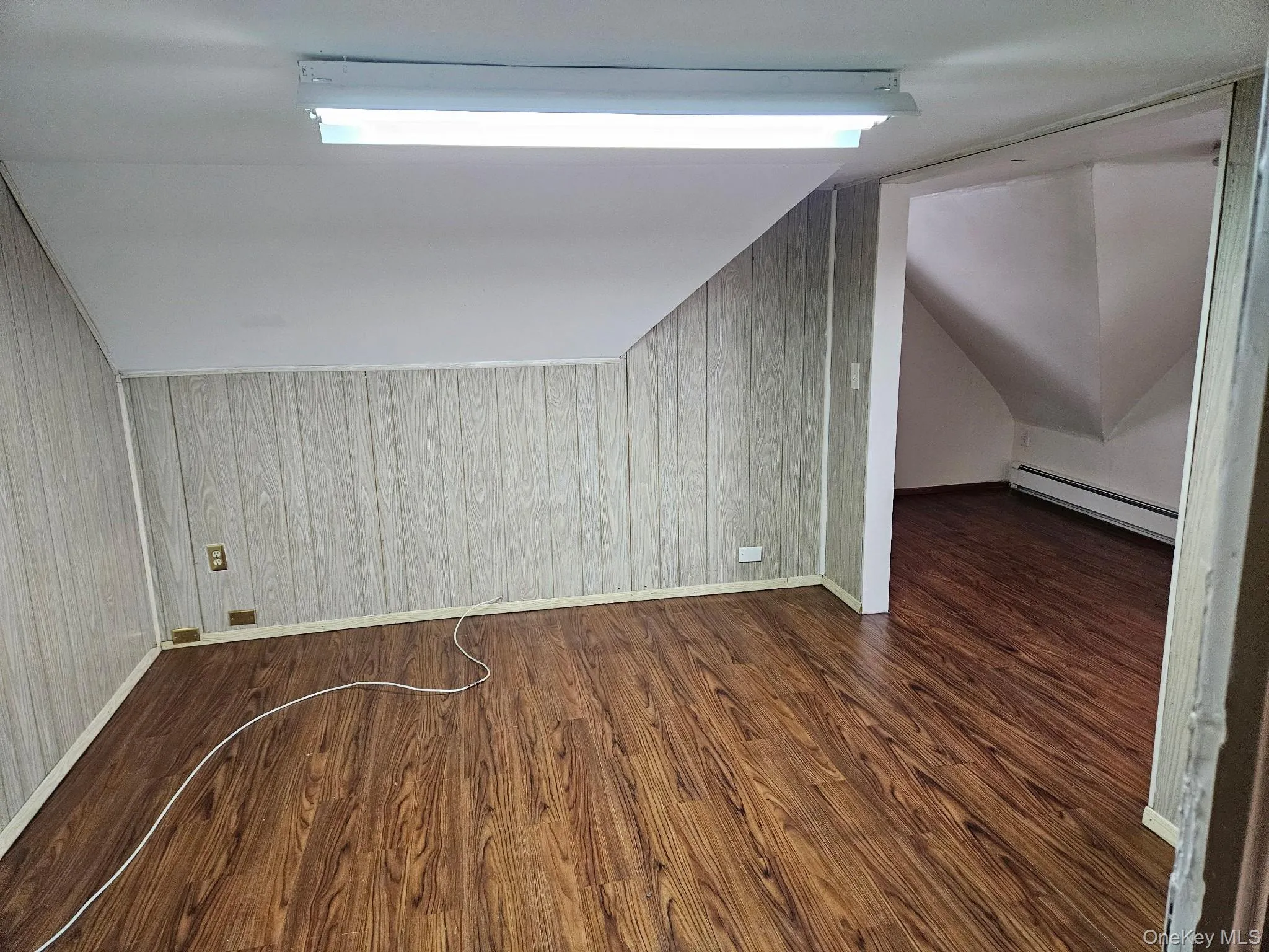 Additional living space featuring dark wood-style flooring, wooden walls, a baseboard radiator, and vaulted ceiling Additional living space featuring dark wood-style flooring, wooden walls, a baseboard radiator, and vaulted ceiling