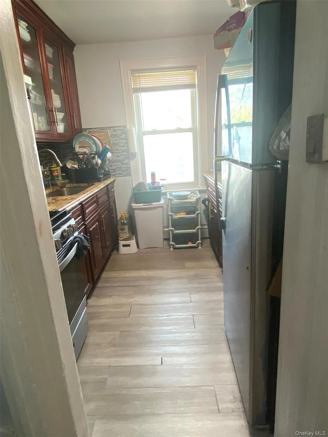 Kitchen with freestanding refrigerator, range with gas cooktop, glass insert cabinets, light wood-style flooring, and decorative backsplash Kitchen with freestanding refrigerator, range with gas cooktop, glass insert cabinets, light wood-style flooring, and decorative backsplash