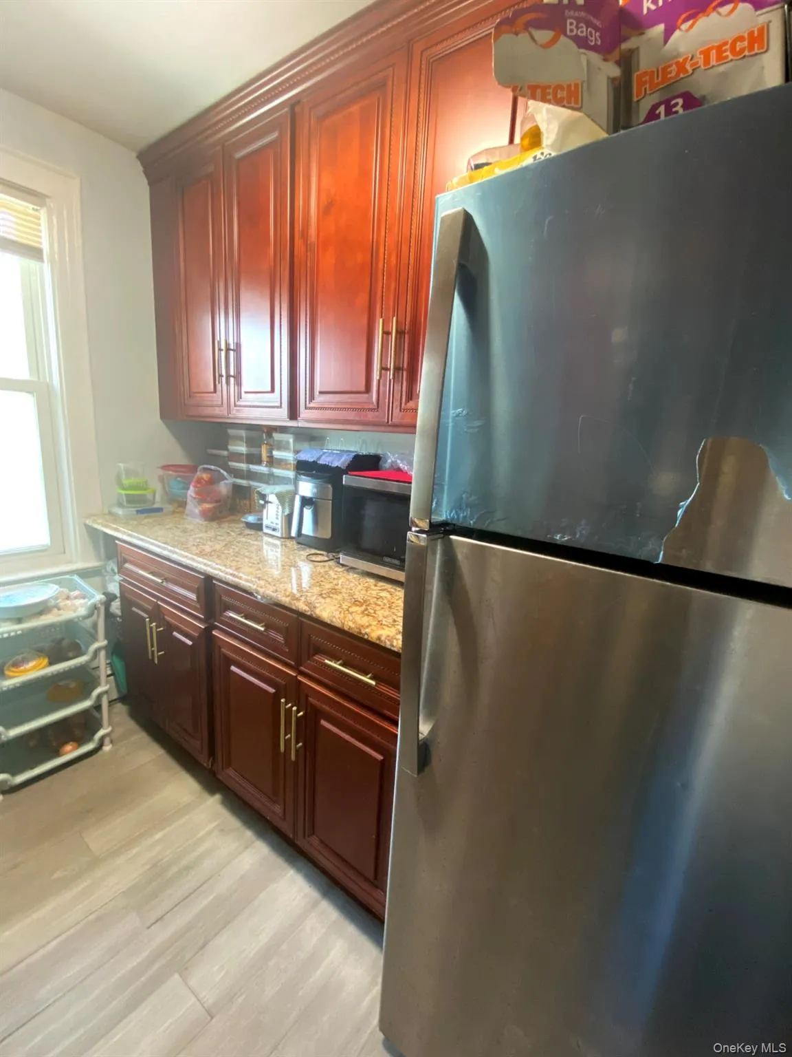 Kitchen featuring appliances with stainless steel finishes, light stone countertops, light wood finished floors, and reddish brown cabinets Kitchen featuring appliances with stainless steel finishes, light stone countertops, light wood finished floors, and reddish brown cabinets