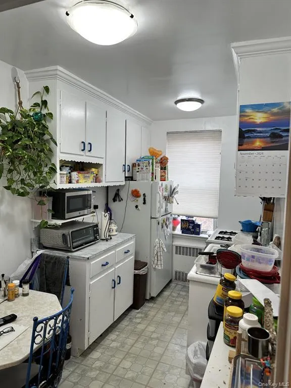 Kitchen featuring light countertops, white cabinets, light floors, freestanding refrigerator, and radiator heating unit Kitchen featuring light countertops, white cabinets, light floors, freestanding refrigerator, and radiator heating unit