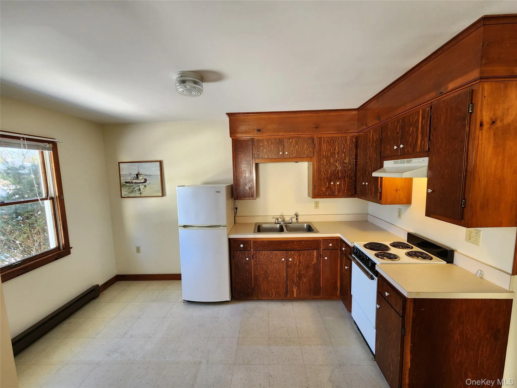 Kitchen with white appliances, light flooring, baseboard heating, light countertops, and under cabinet range hood Kitchen with white appliances, light flooring, baseboard heating, light countertops, and under cabinet range hood