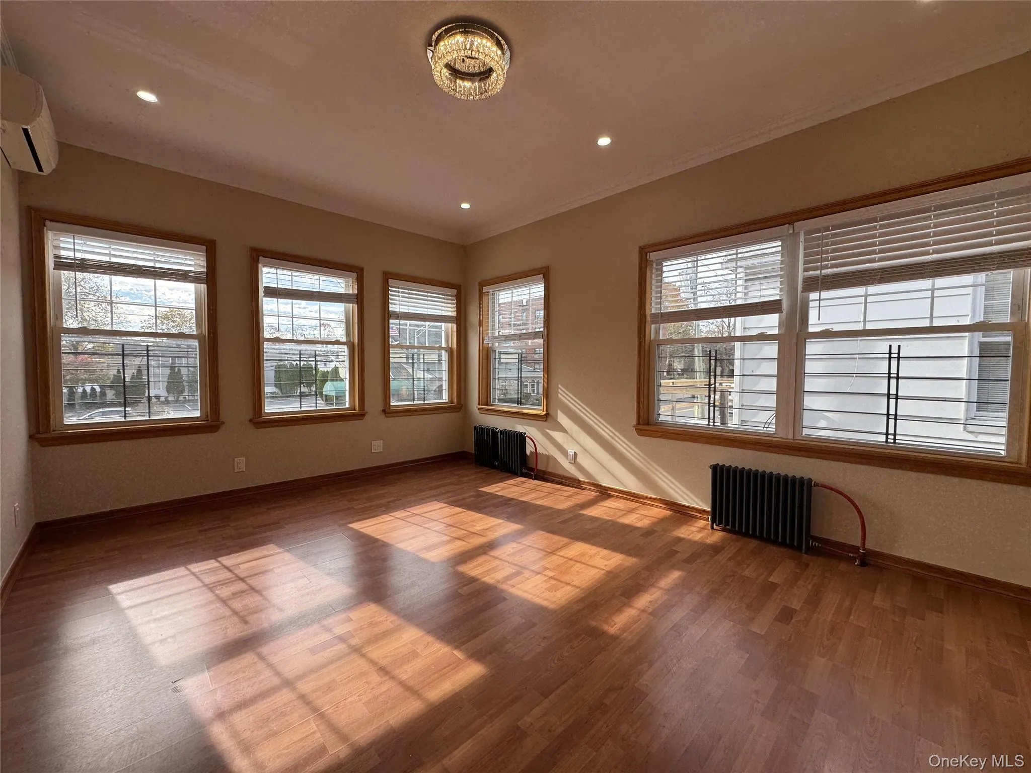 Unfurnished room with healthy amount of natural light, radiator, wood finished floors, and recessed lighting Unfurnished room with healthy amount of natural light, radiator, wood finished floors, and recessed lighting