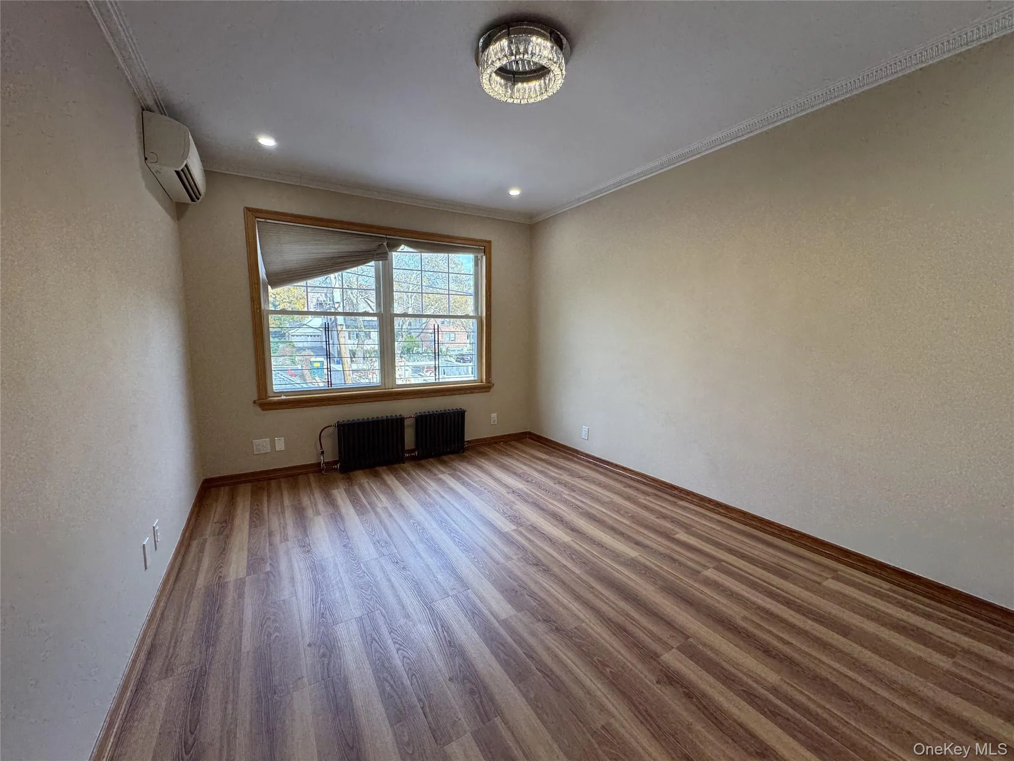 Spare room with wood finished floors, a textured wall, an AC wall unit, crown molding, and radiator Spare room with wood finished floors, a textured wall, an AC wall unit, crown molding, and radiator